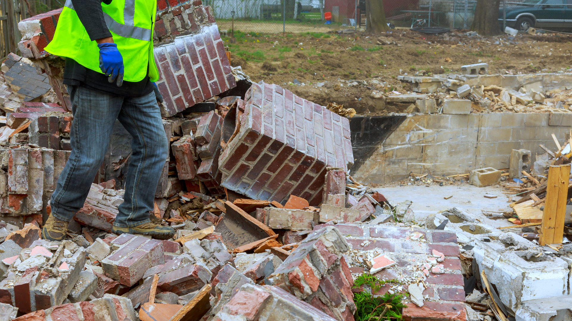 Construction worker in neon vest standing amid collapsed brick rubble at a muddy demolition site