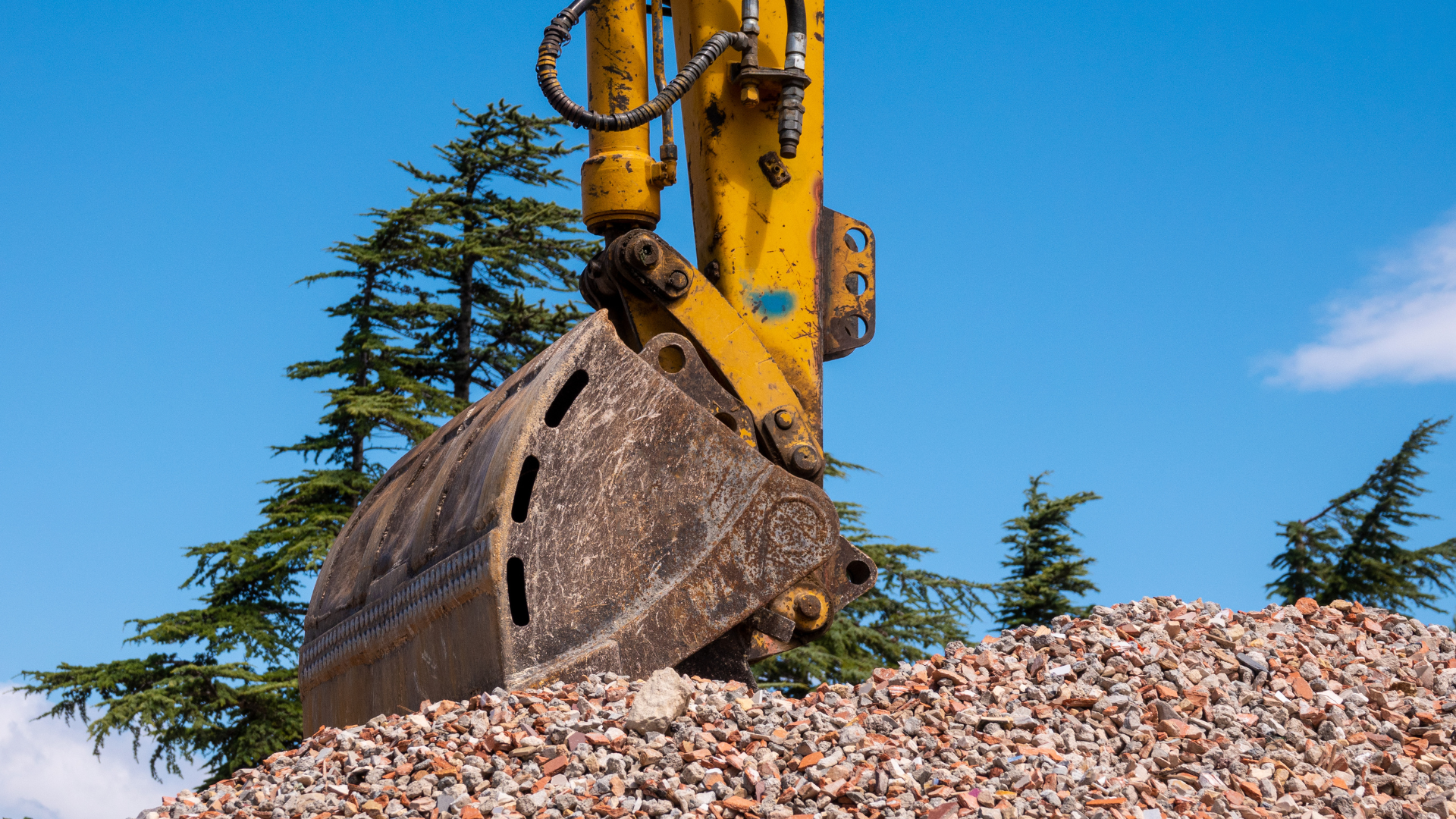 A yellow excavator is digging a pile of gravel.