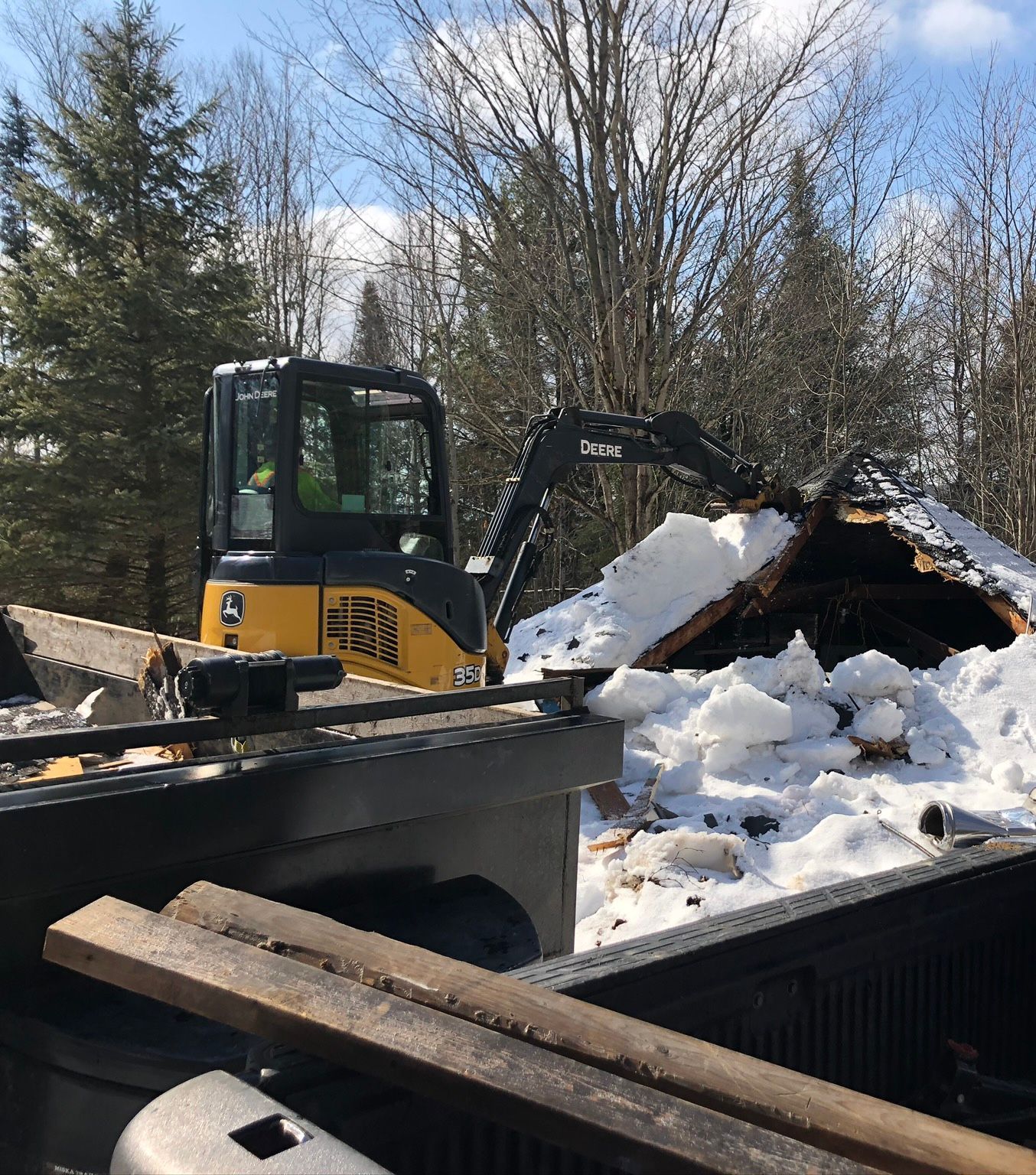 A yellow and black excavator is sitting on top of a pile of snow.