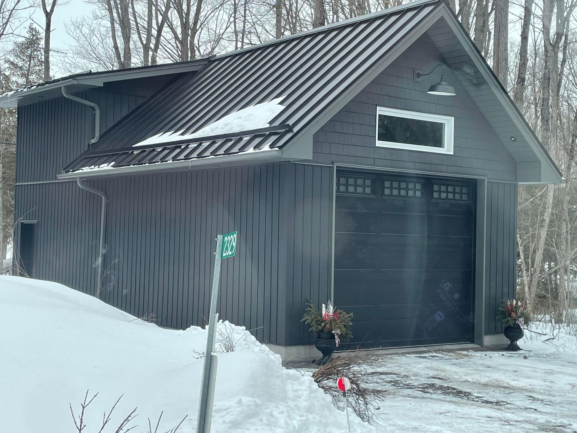 A black garage with a metal roof is surrounded by snow.