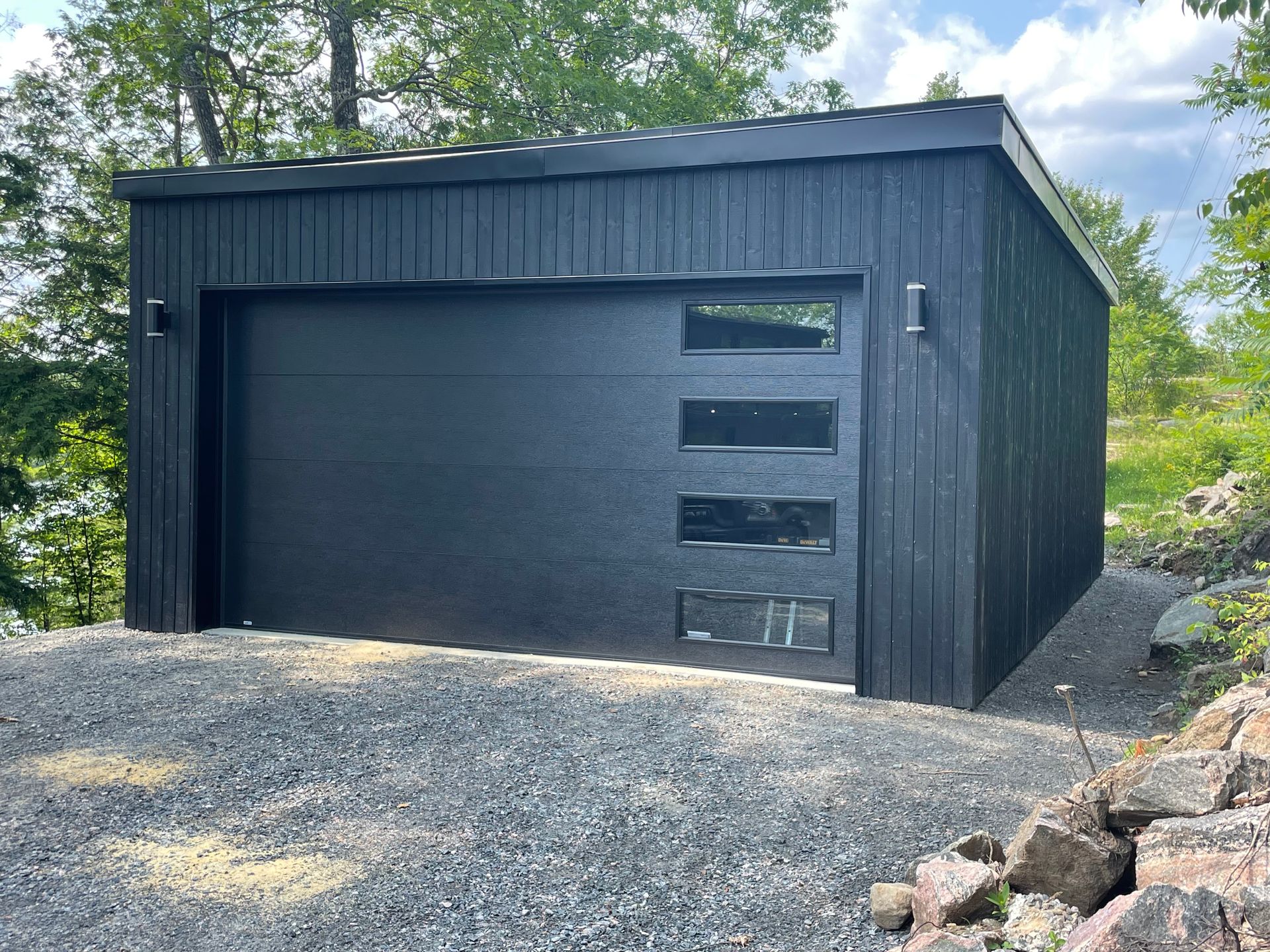A black garage with a black garage door is sitting on top of a gravel hill.