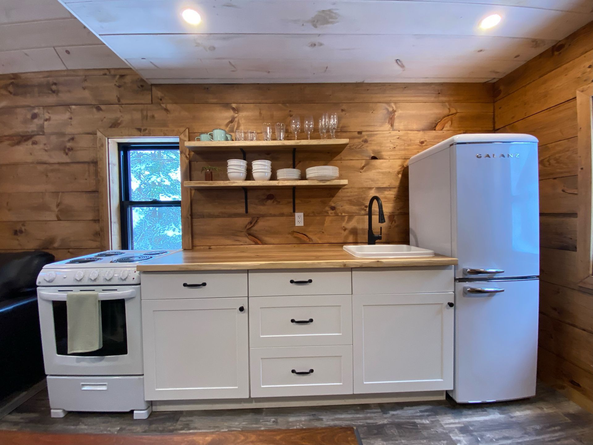 A kitchen with white cabinets , a stove , a refrigerator and a sink.