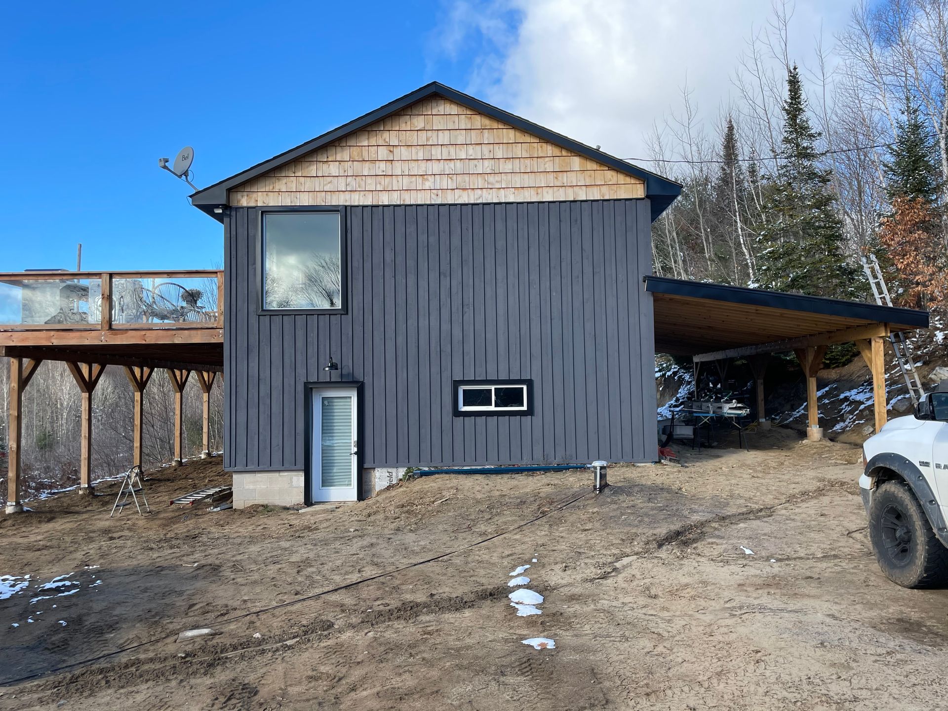 A black house with a carport and a white truck parked in front of it.