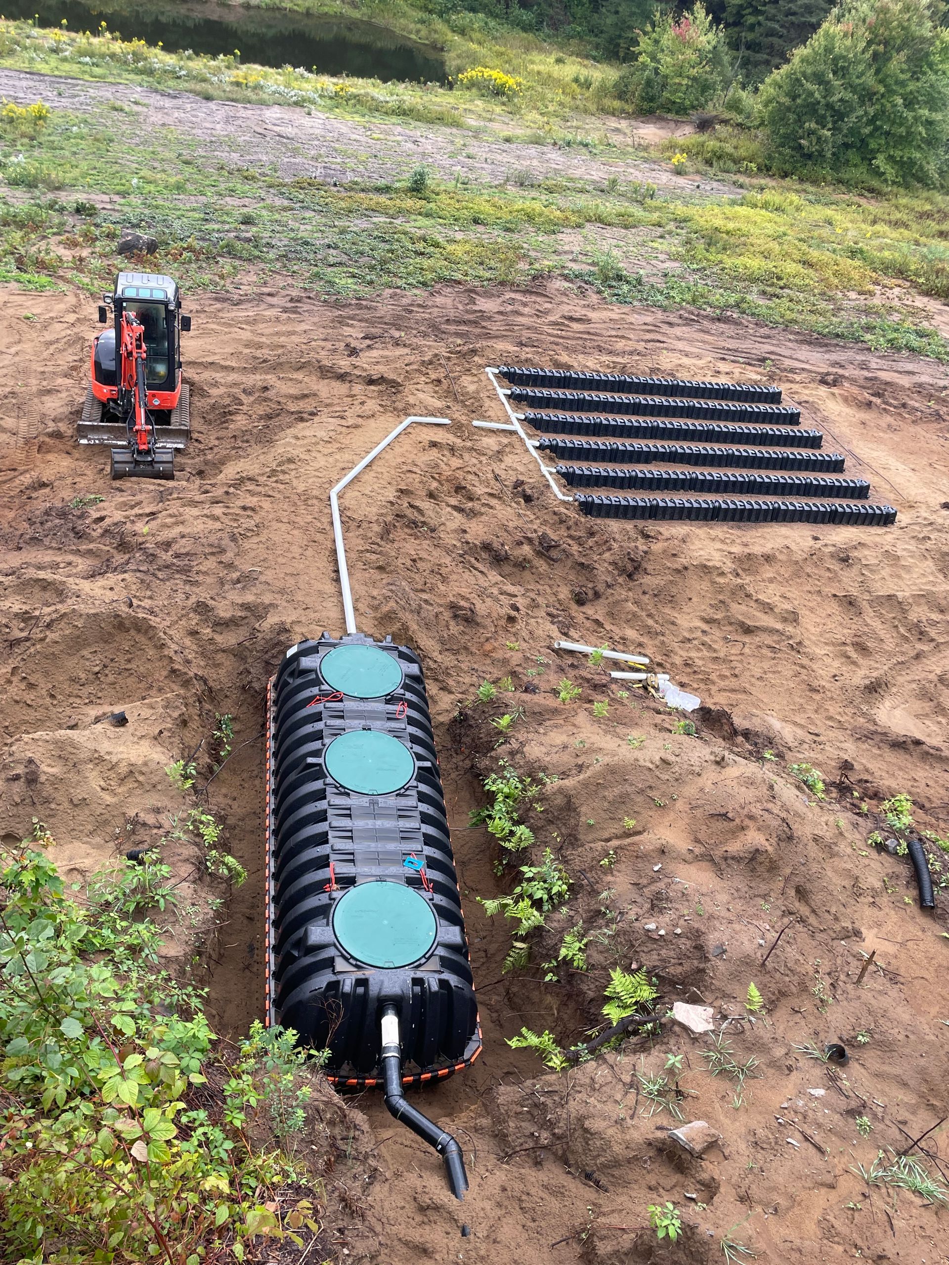 A large black tank is sitting in the middle of a dirt field next to a small excavator.