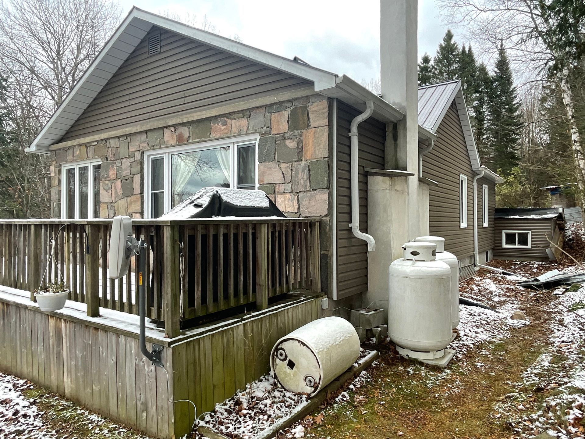 A small house with a deck and a propane tank in front of it.