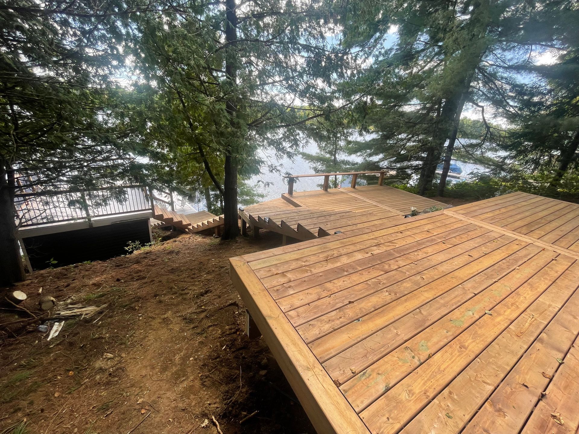 A wooden deck with stairs leading up to a lake surrounded by trees.