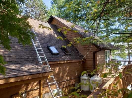 A house with a ladder on the side of it and a skylight on the roof.