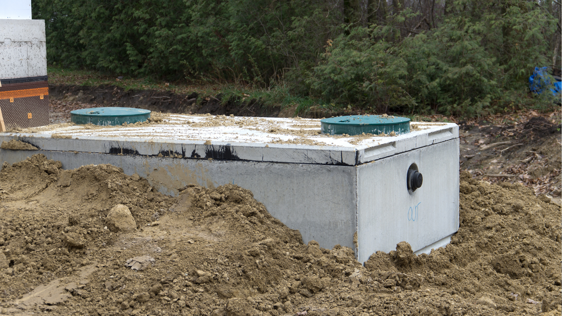 A concrete septic tank with two green access lids, partially buried in dirt.