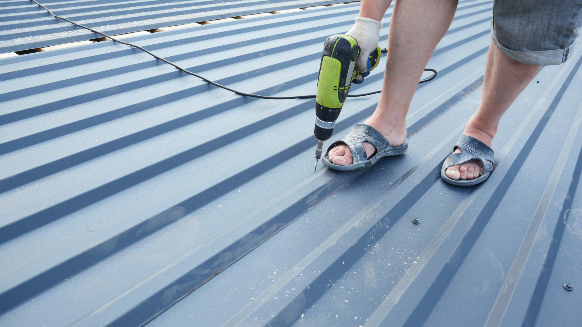 A man is using a drill on a metal roof.