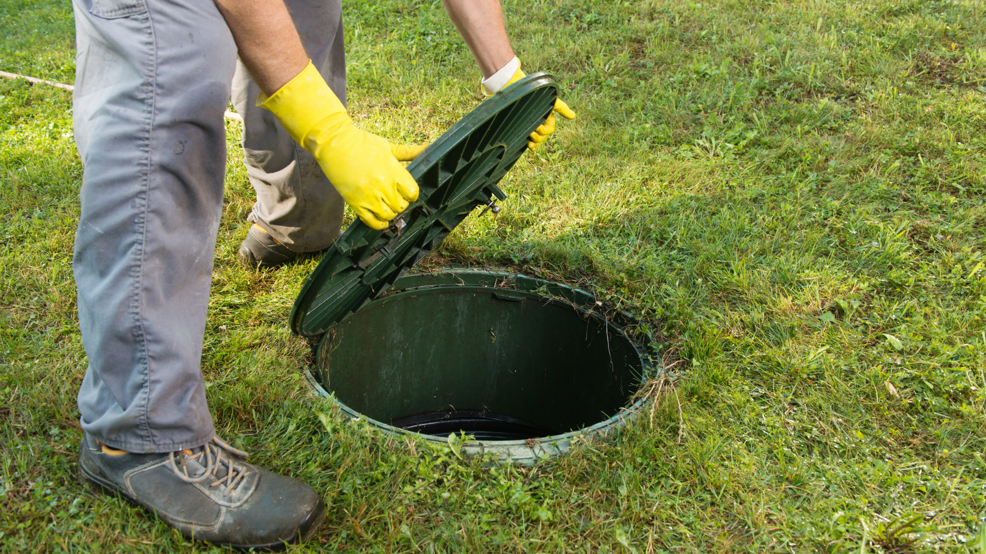 A man wearing yellow gloves is opening a septic tank.