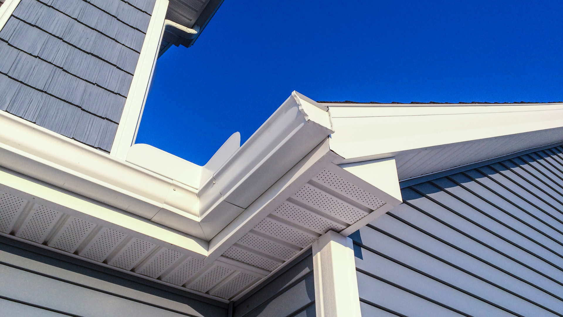 A white gutter on the side of a house with a blue sky in the background.