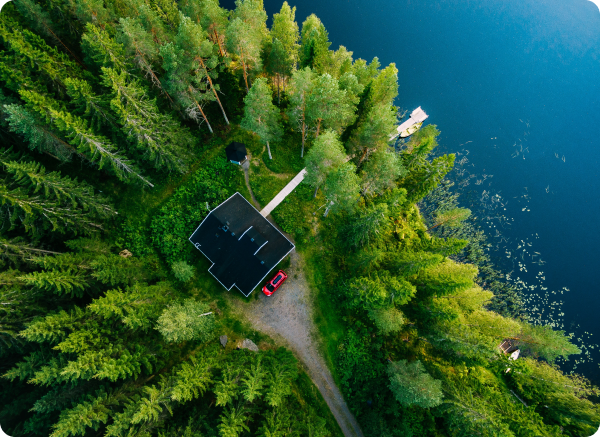 An aerial view of a house in the middle of a forest next to a lake.