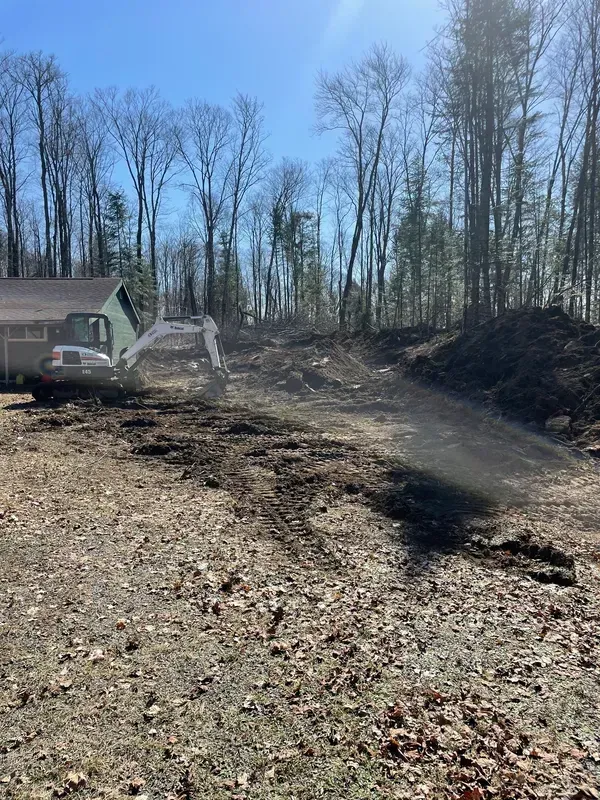 A bulldozer is clearing a dirt road in front of a house.