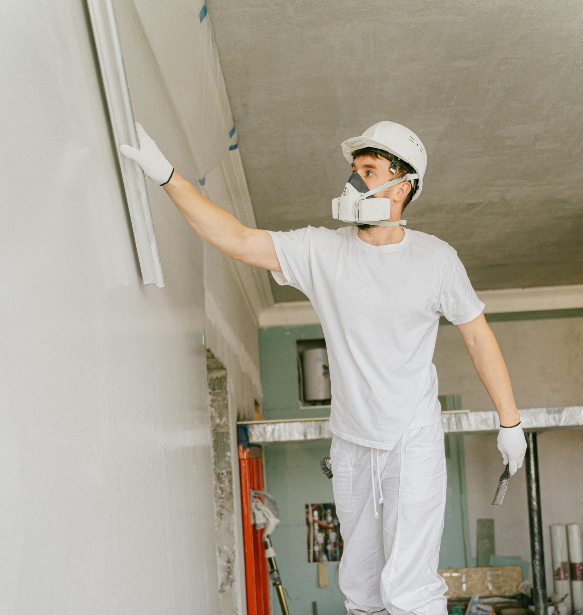 Person in protective gear, smoothing plaster on a wall during construction.