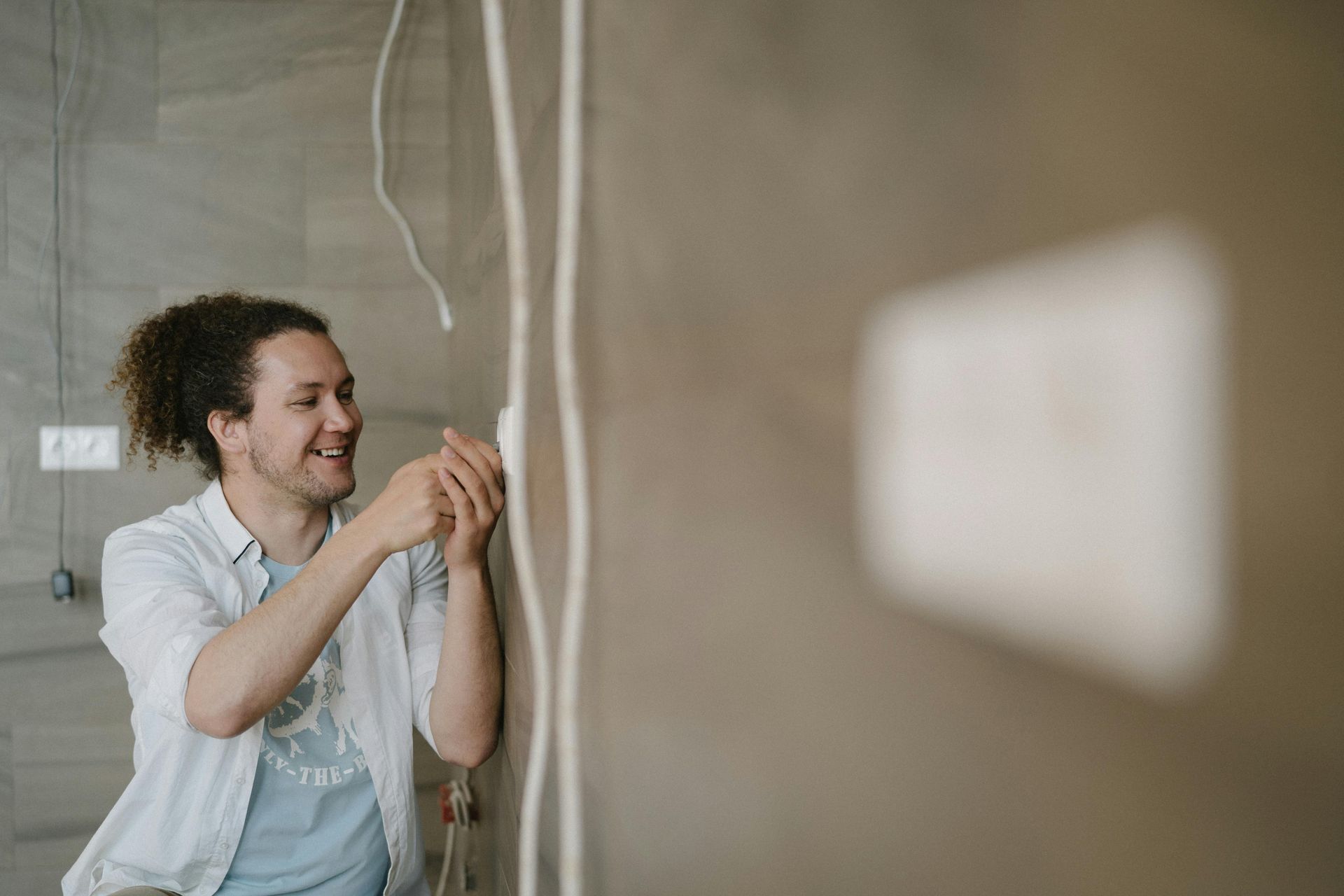 Man smiles while working on wiring on a wall; setting with unfinished walls.