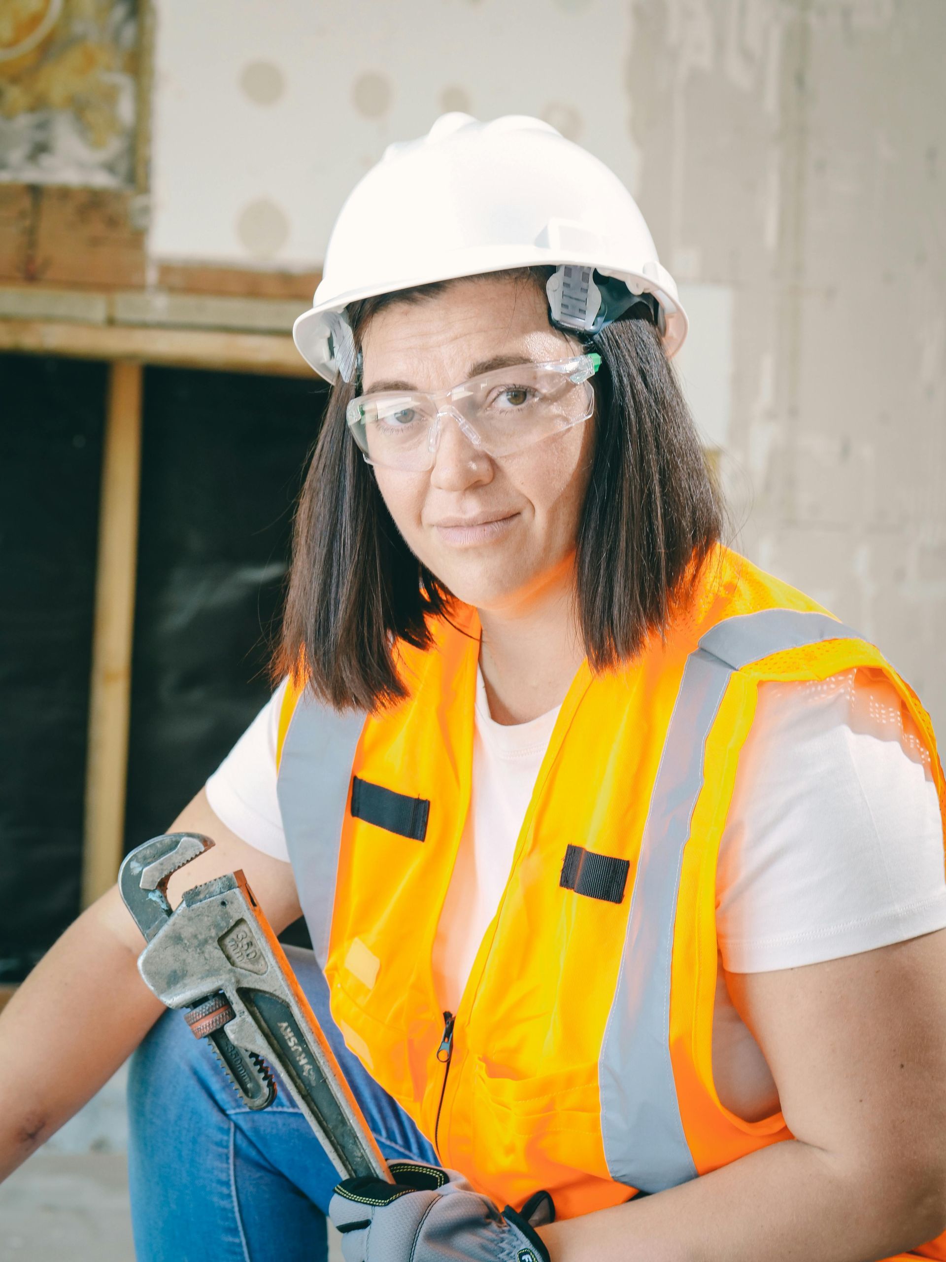 Woman in safety gear holding a wrench, posing in a construction setting.