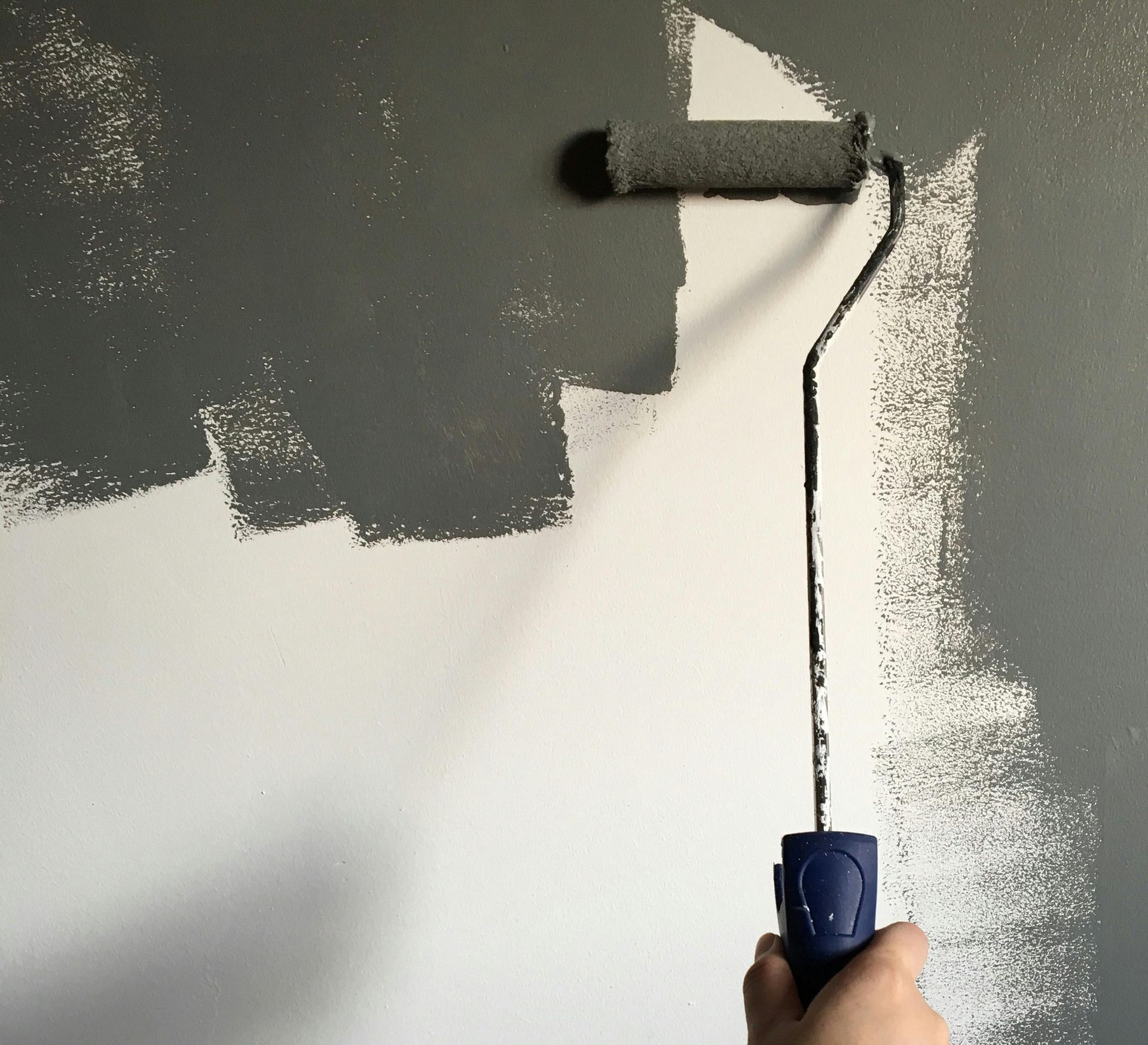 Painting a gray wall with a paint roller, showing a color contrast.
