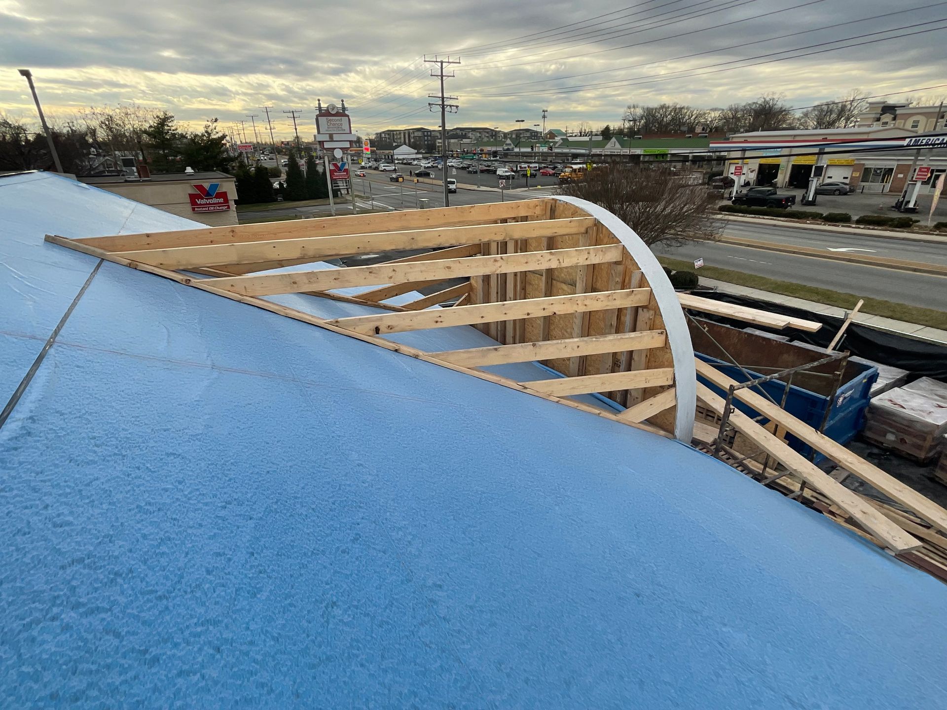 Construction site with exposed wooden roof beams, blue insulation, and city street in the background.