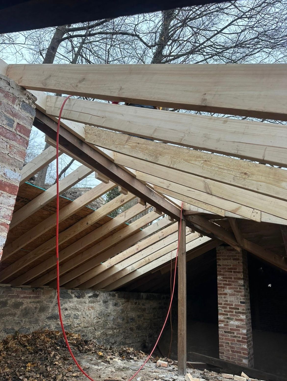 Construction of a roof framework, with wooden beams and planks, against a brick structure.