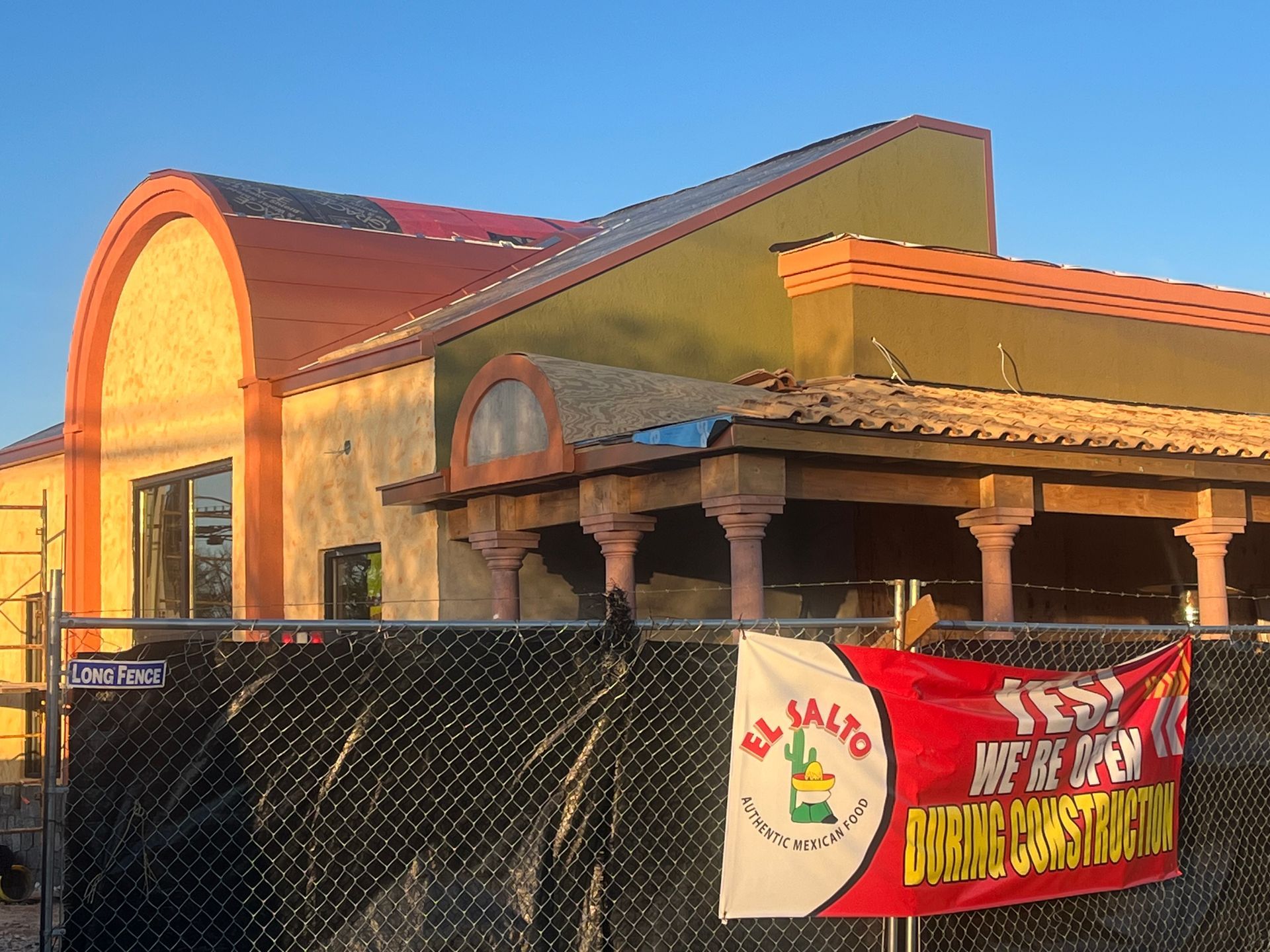 Building with arched roof and pillars behind a chain link fence. Banner: 