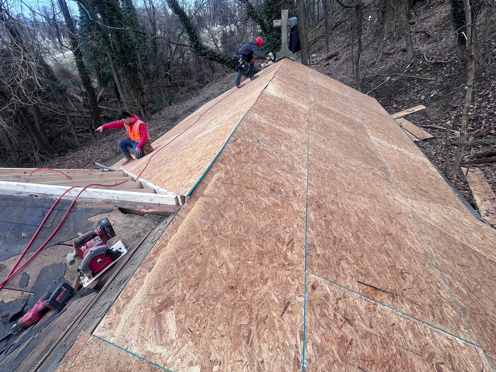 Construction workers installing roofing on a church building; cross on the roof.