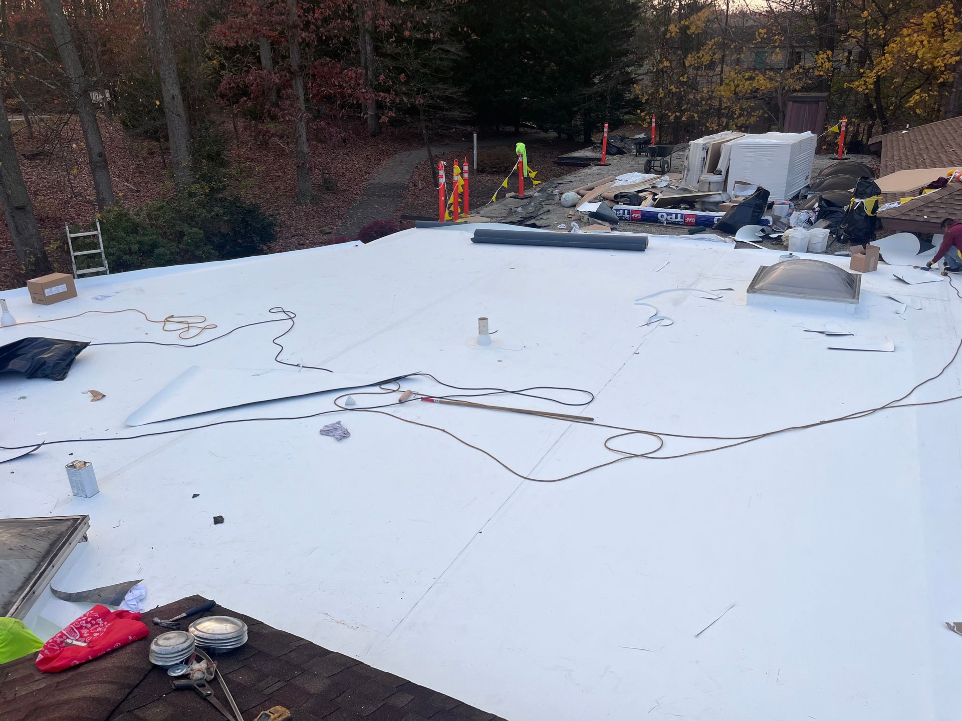 White roofing material being installed on a low-slope roof, with several workers and supplies visible.