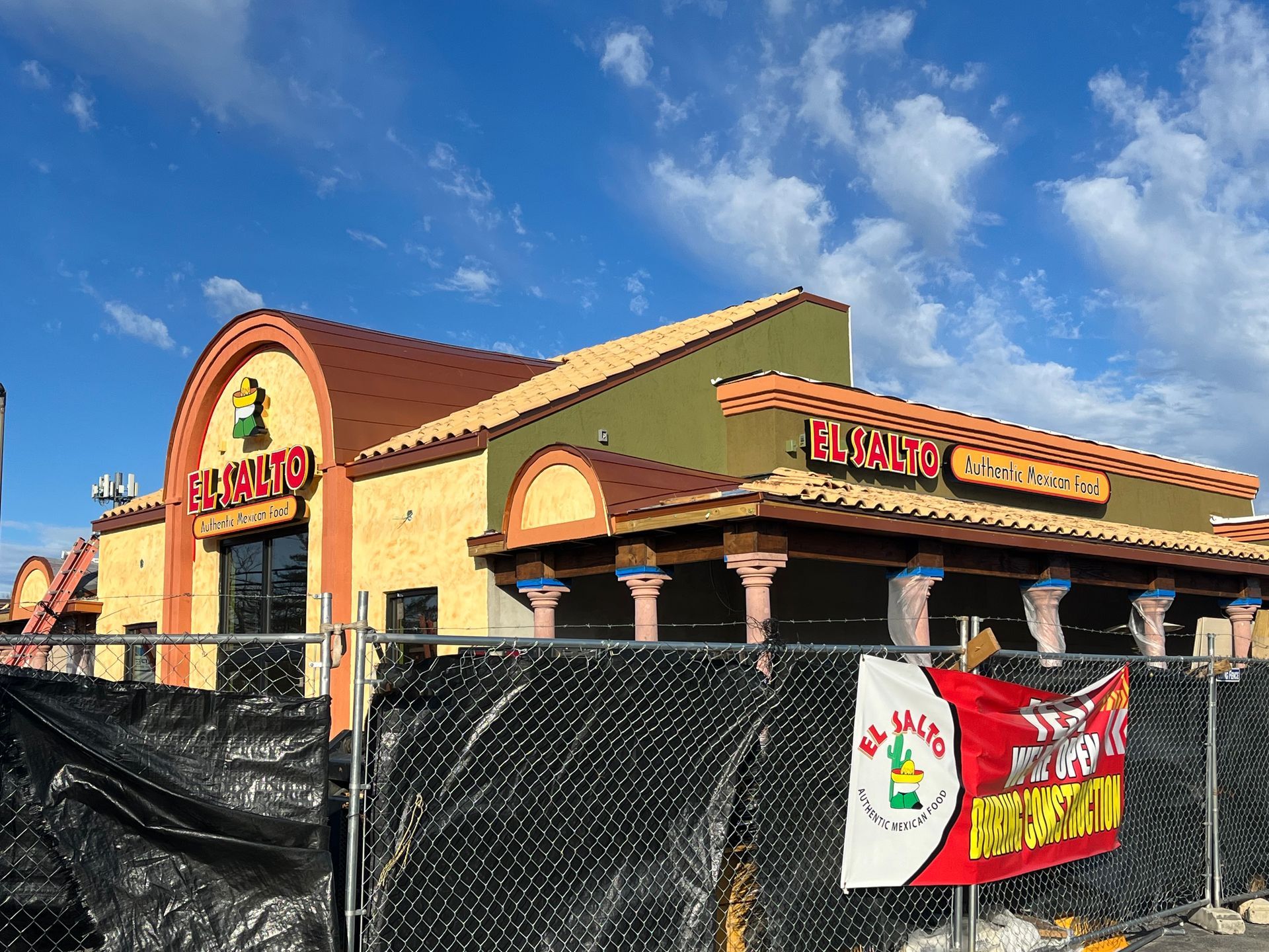 Construction site of El Salto restaurant; yellow and brown stucco, brown roof. Fence in front with banner.