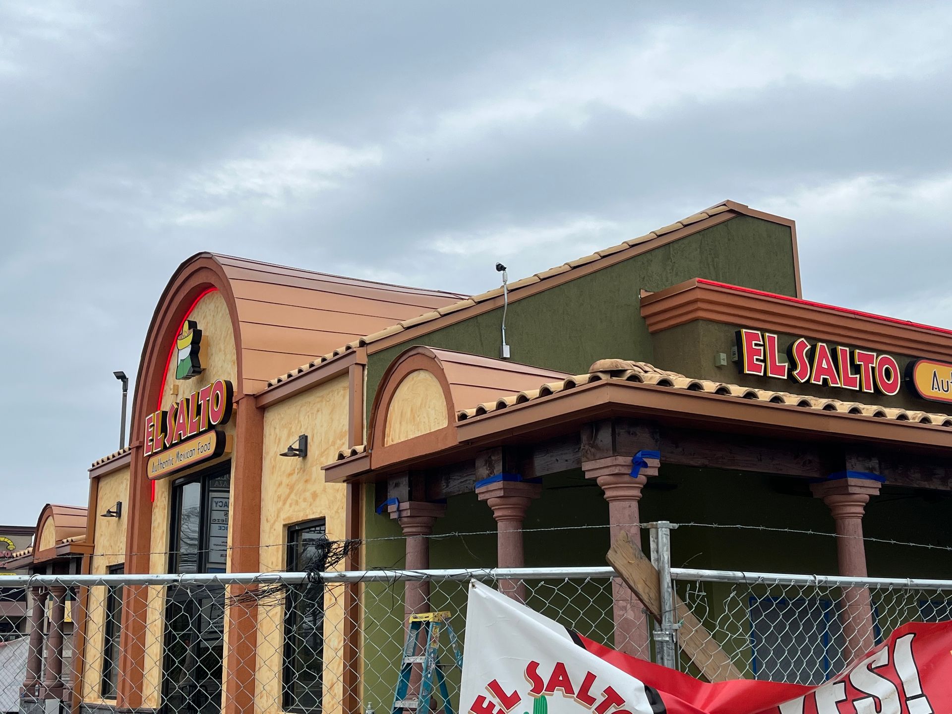 Exterior of El Salto restaurant under overcast sky, with terracotta tile roof and red and gold signage.