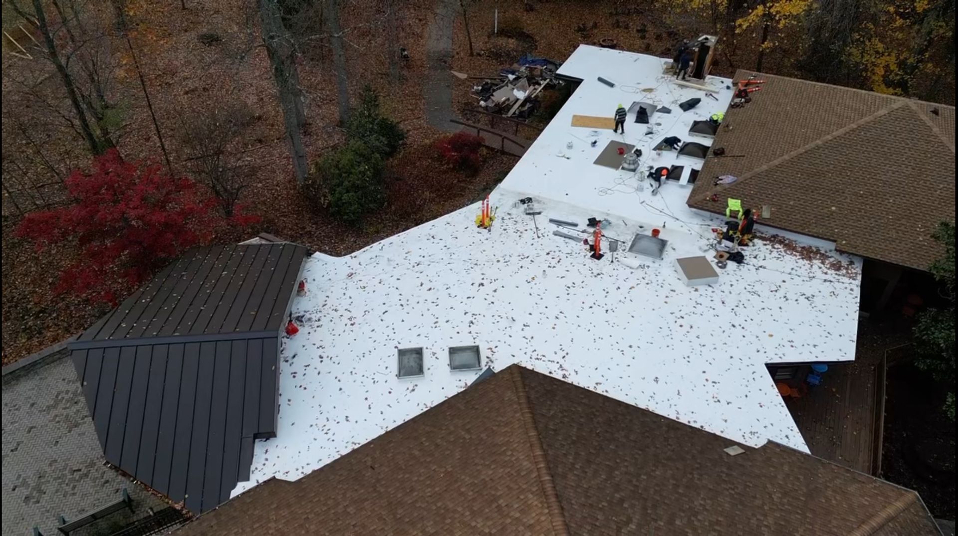 Aerial view of a roof being replaced with workers present. White material covers most of the surface. 