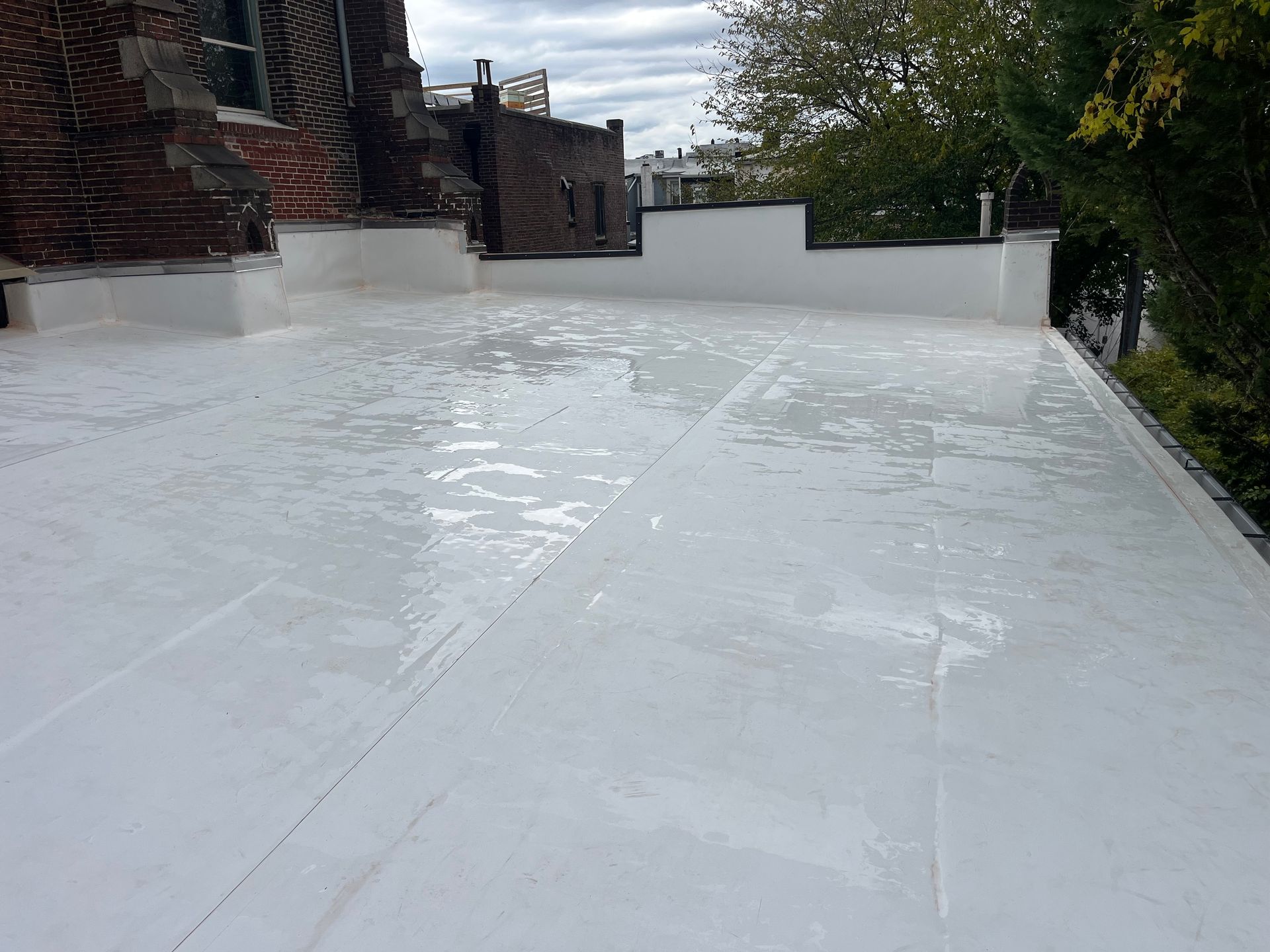 White coated flat roof, likely recently sealed, with low brick buildings visible. Cloudy sky.