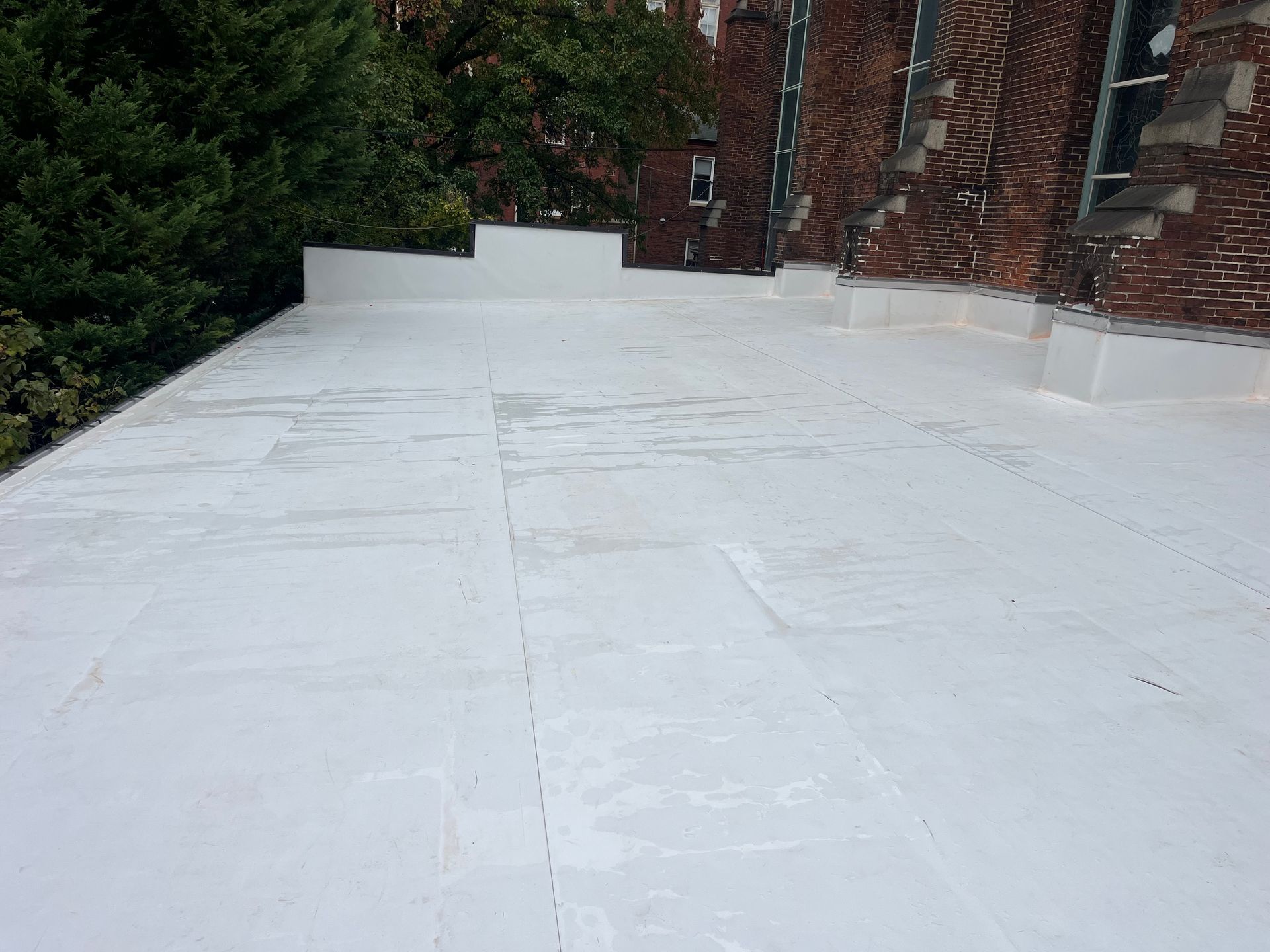 White flat roof on a brick building with visible seams. Trees in the background.