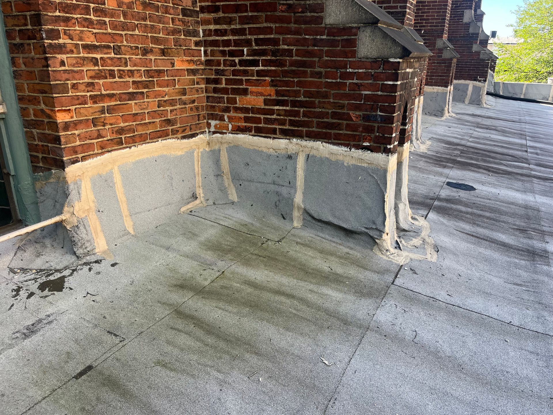 Flat roof with brick wall, showing tar and repairs. Gray roof, brown brick.