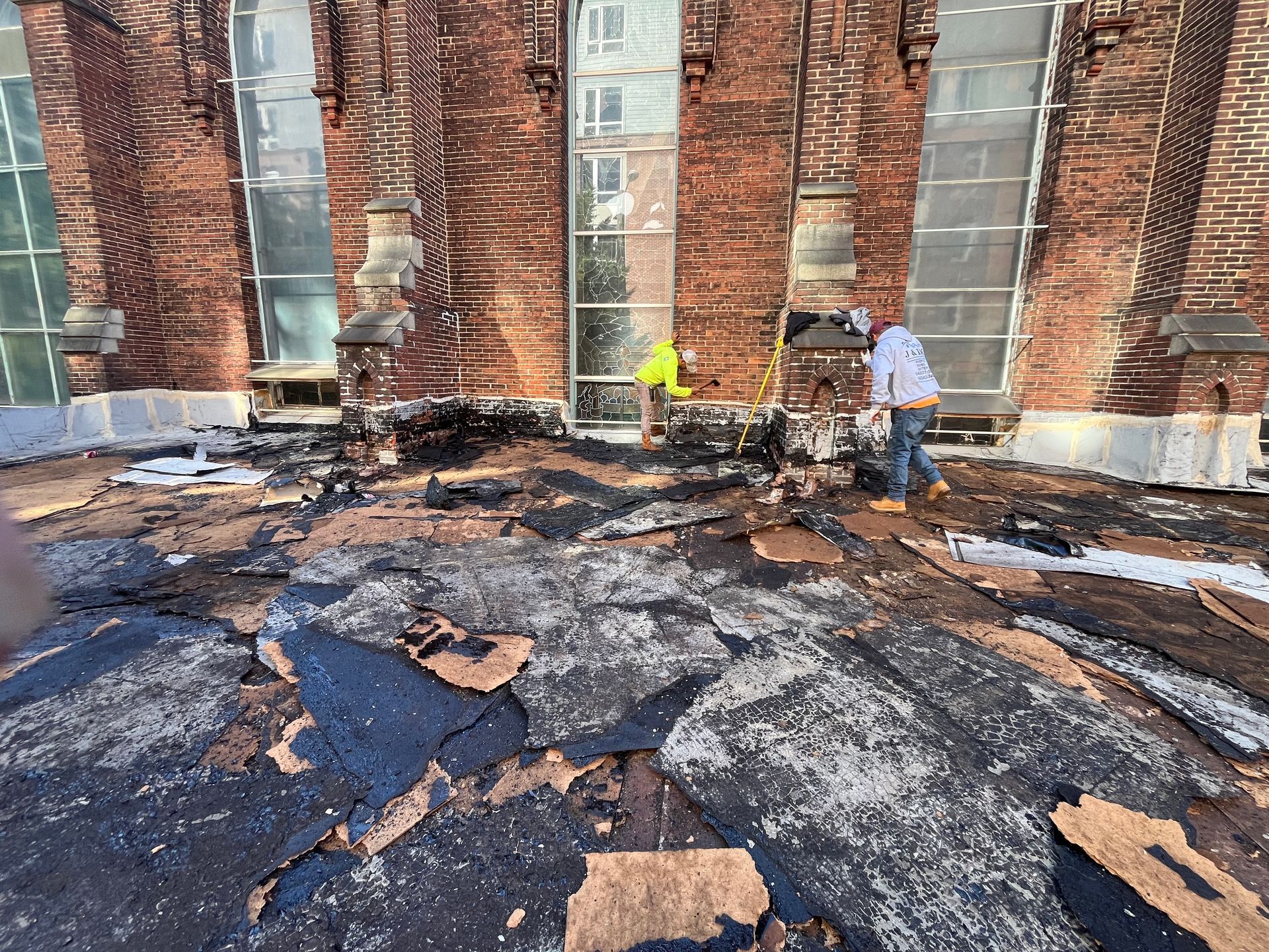 Roof repair with workers, exposed black and white materials, red brick building, sunny day.