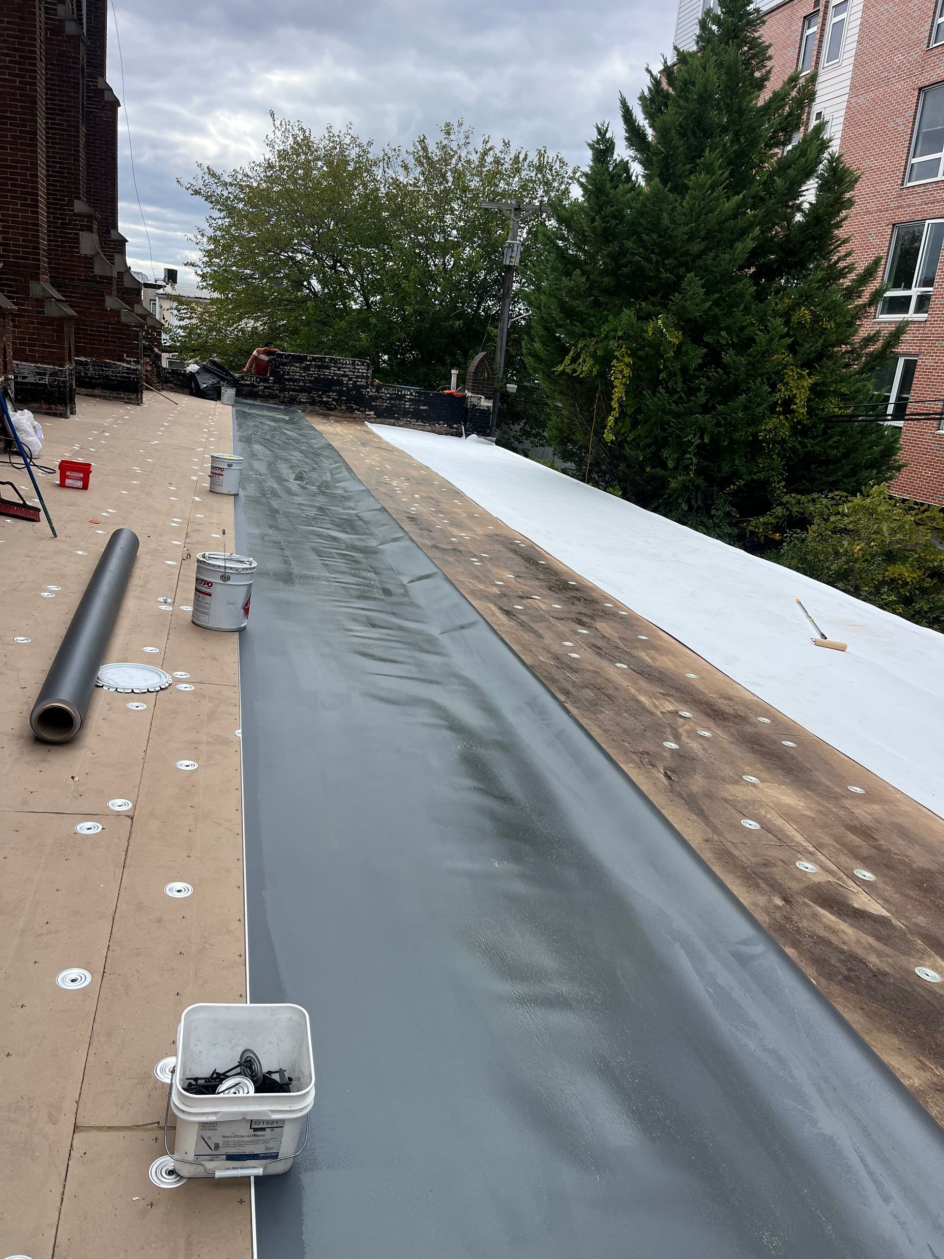 Roofing project: applying gray sealant to a flat roof, white sections of roofing material.