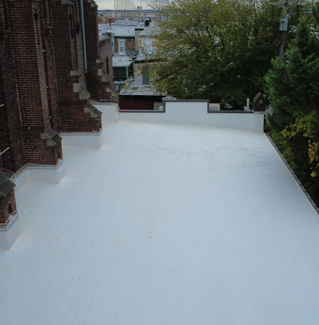 Flat white roof with brick structure on the left, trees in background.
