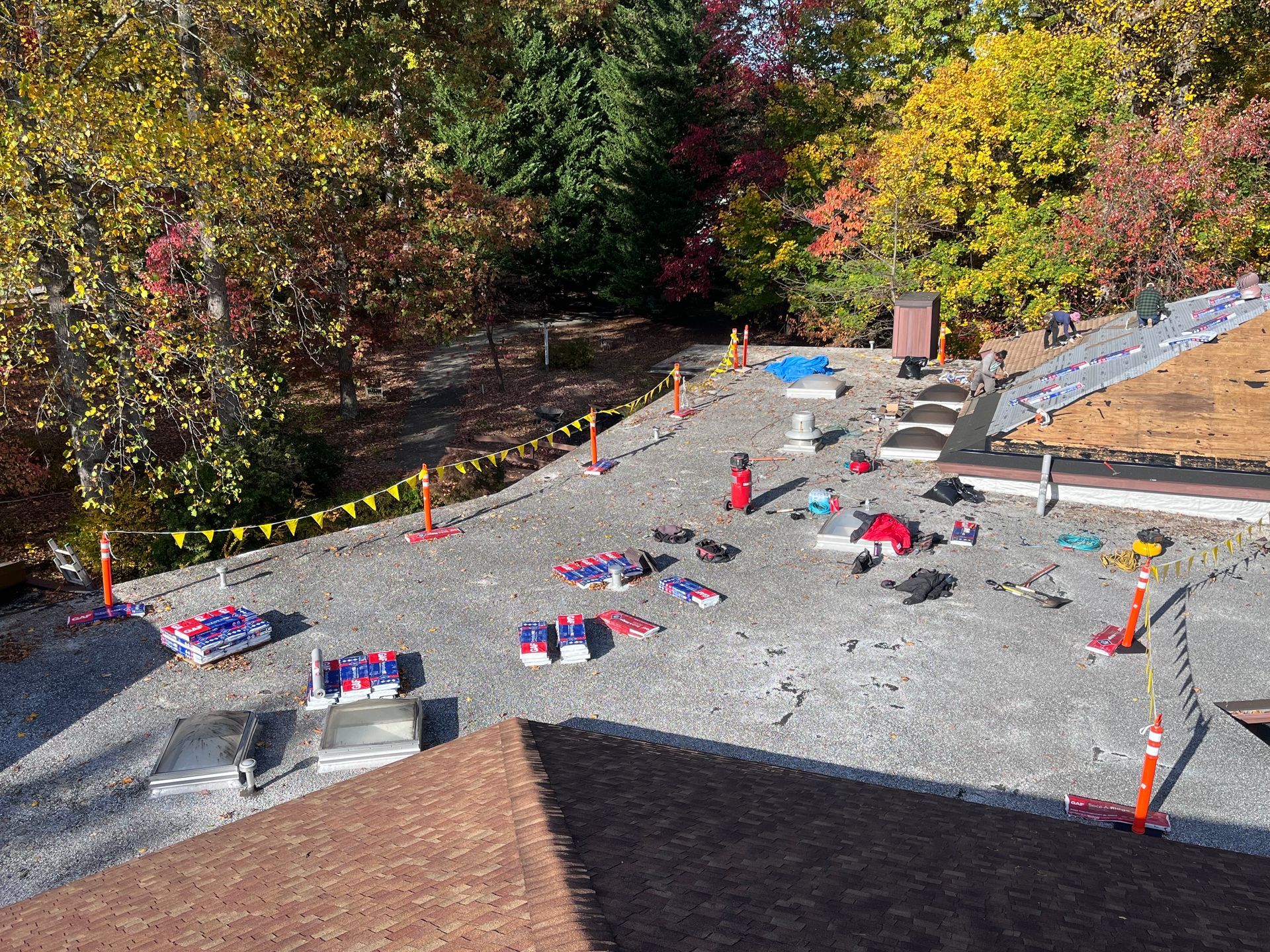 Rooftop with gravel, construction materials, and safety equipment, surrounded by trees with autumn foliage.