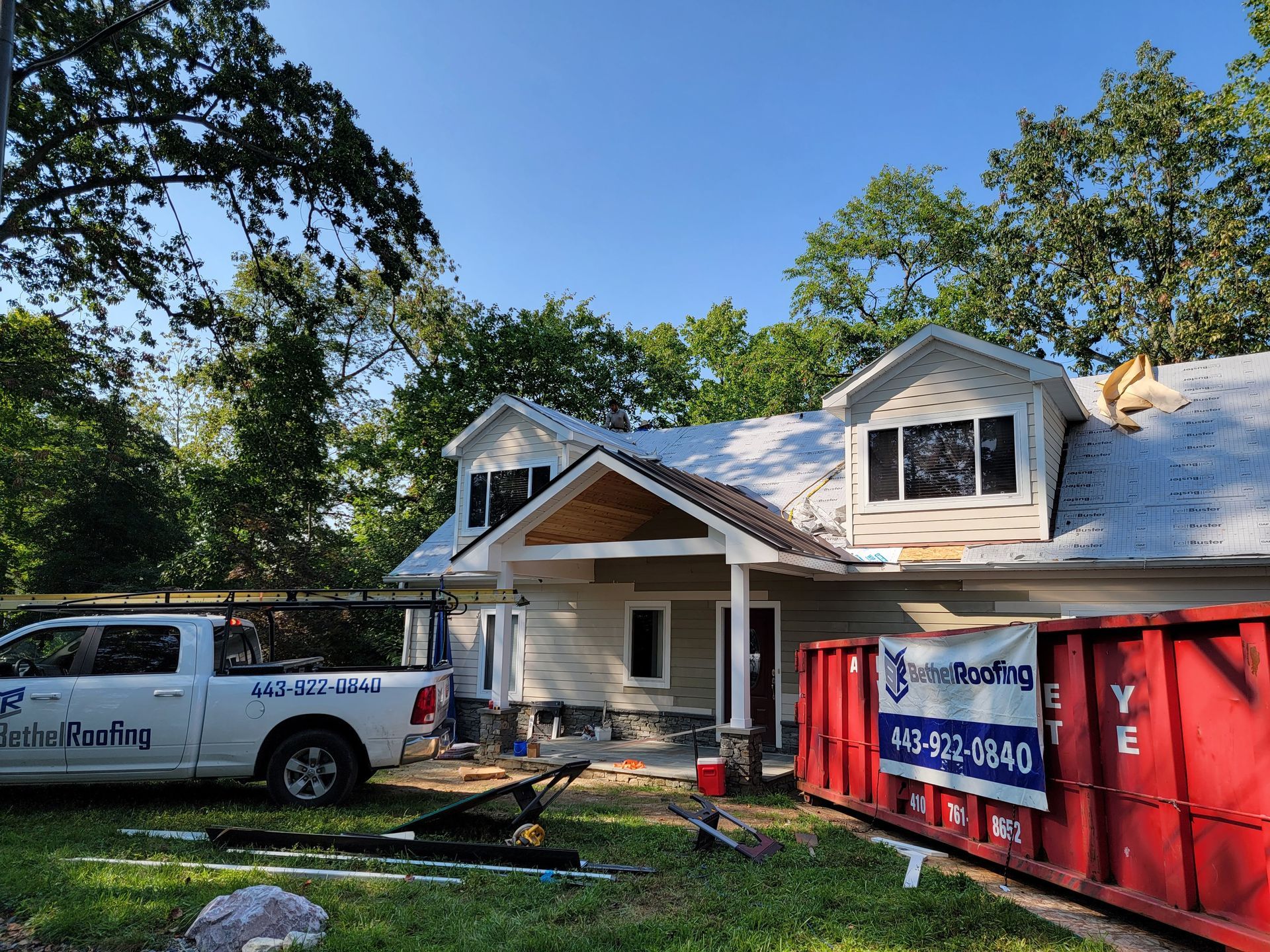 House with new roof under construction; white truck and red dumpster in yard.