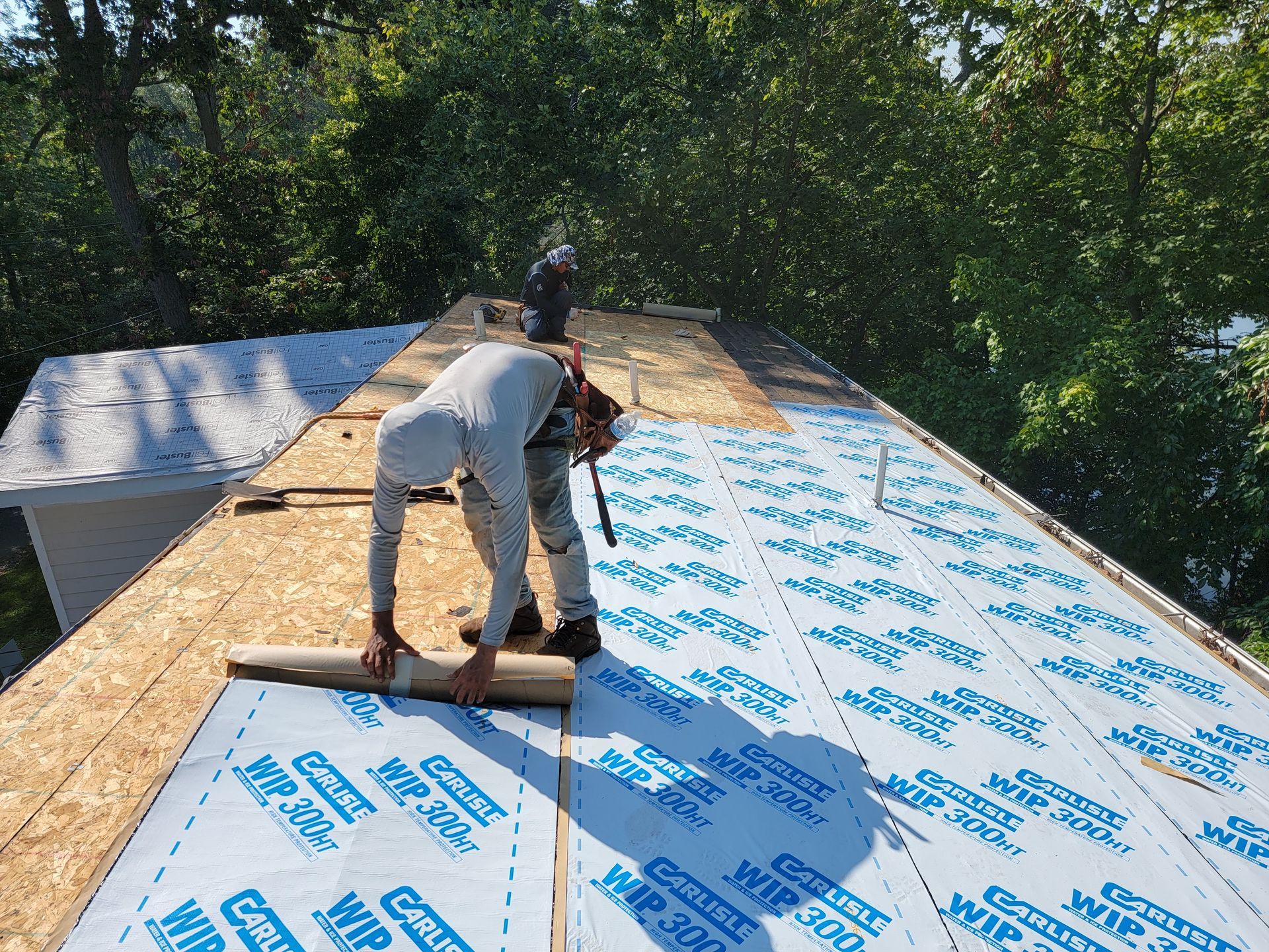 Construction worker installing roofing material on a house roof on a sunny day.