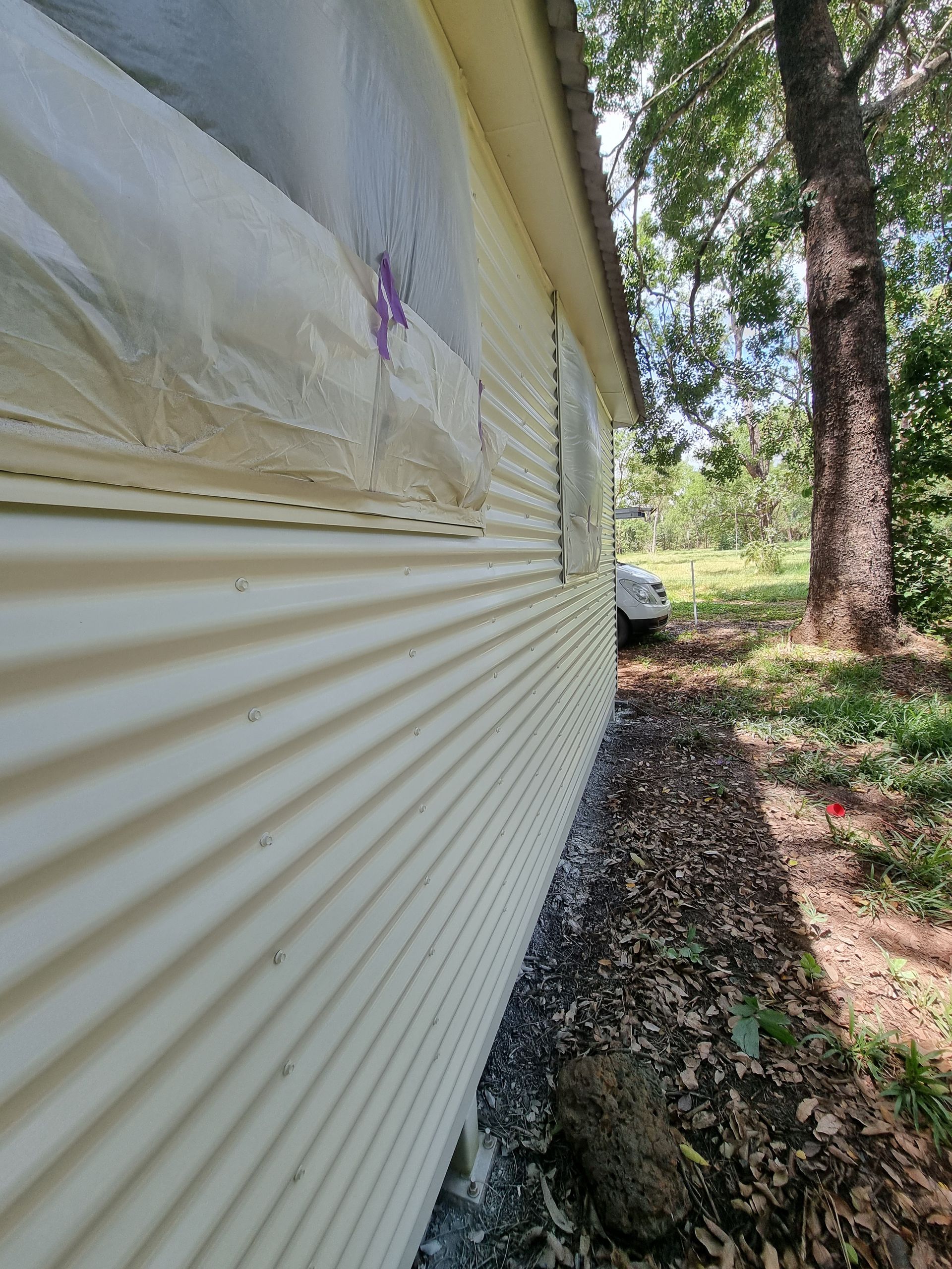 Beige Corrugated Siding on a Building With a Window Covered in Plastic — Prestige Painting NT in Zuccoli, NT