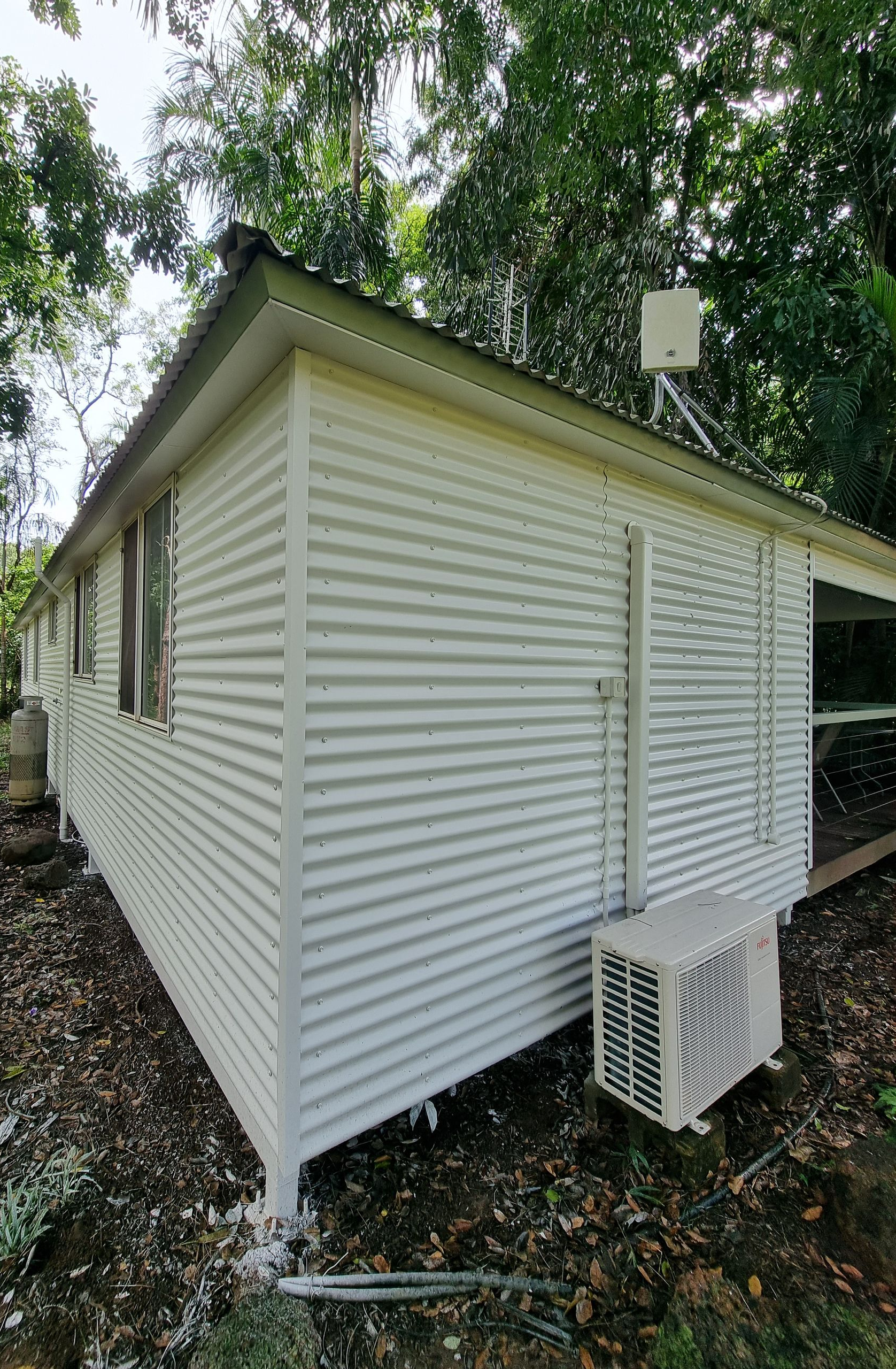 White corrugated metal building in a leafy setting; AC unit visible.  — Prestige Painting NT in Zuccoli, NT