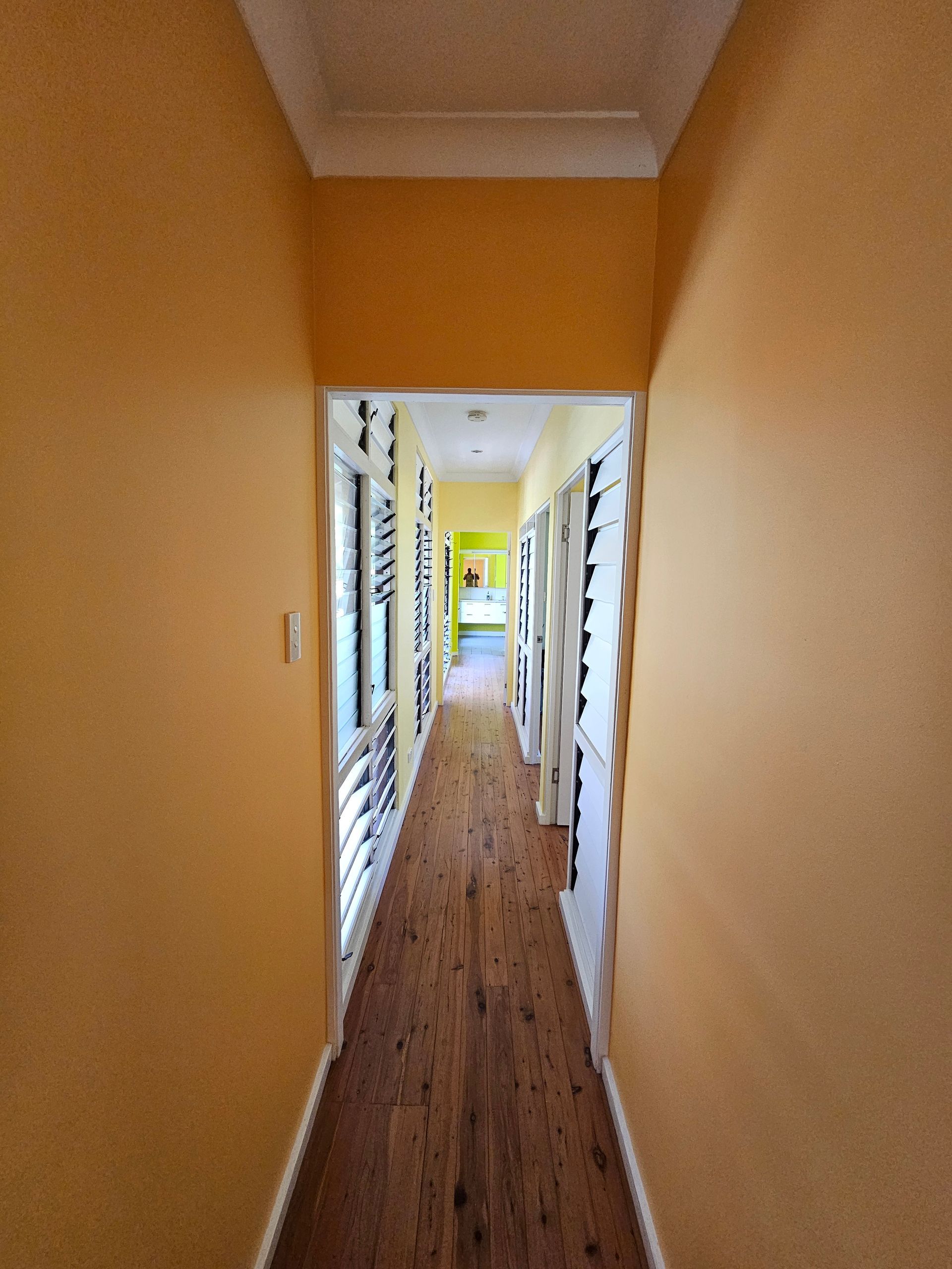 Narrow hallway with yellow walls, wood floor, and doors. — Prestige Painting NT in Zuccoli, NT