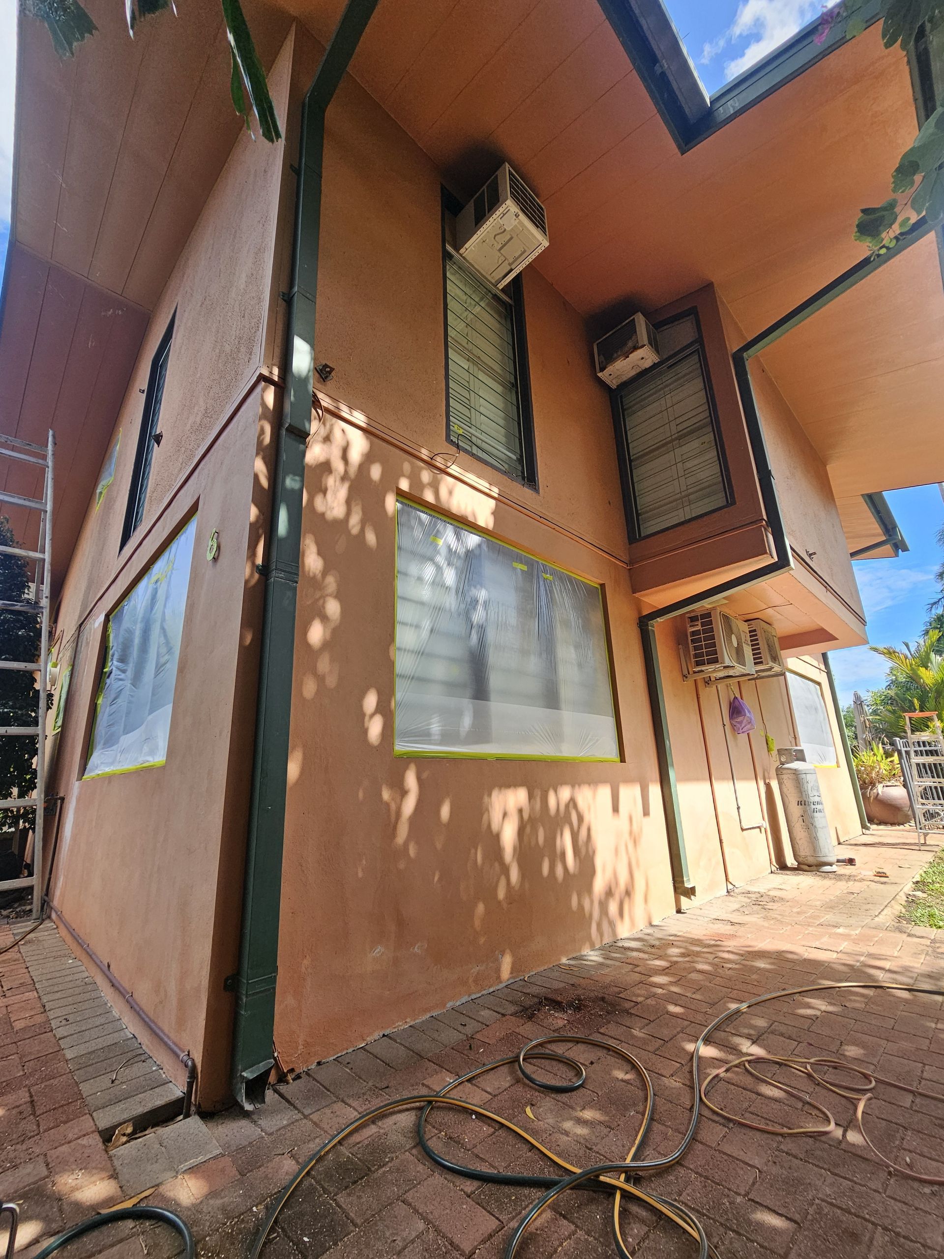 Tan building with dark green trim and AC units. Windows are taped. — Prestige Painting NT in Zuccoli, NT