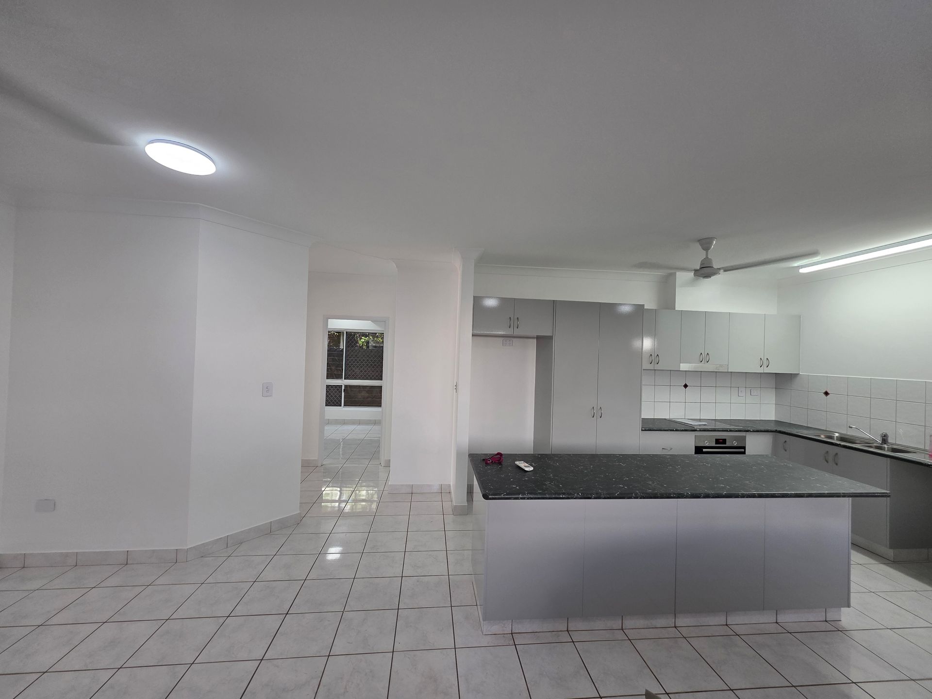 Open-plan kitchen with white walls, gray cabinets, a dark countertop island, and tile floors.— Prestige Painting NT in Zuccoli, NT