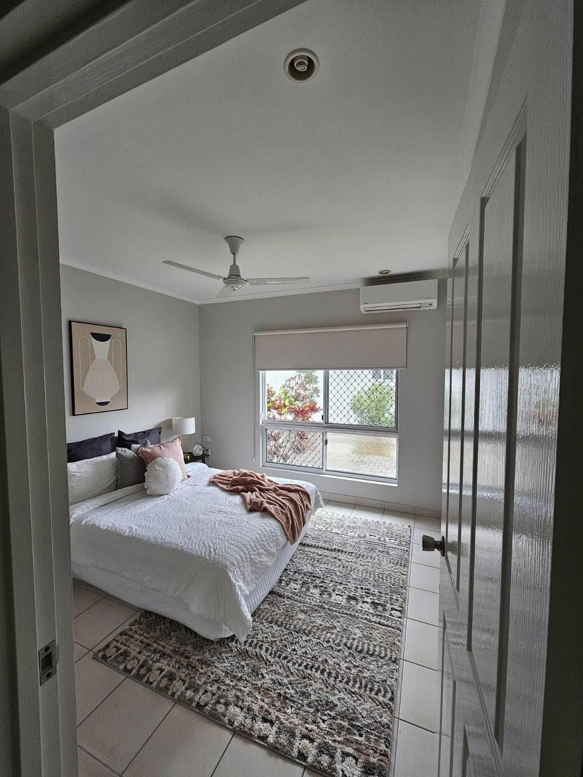 Bedroom with bed, rug, window, and closed door. Light colors, neutral decor. — Prestige Painting NT in Zuccoli, NT