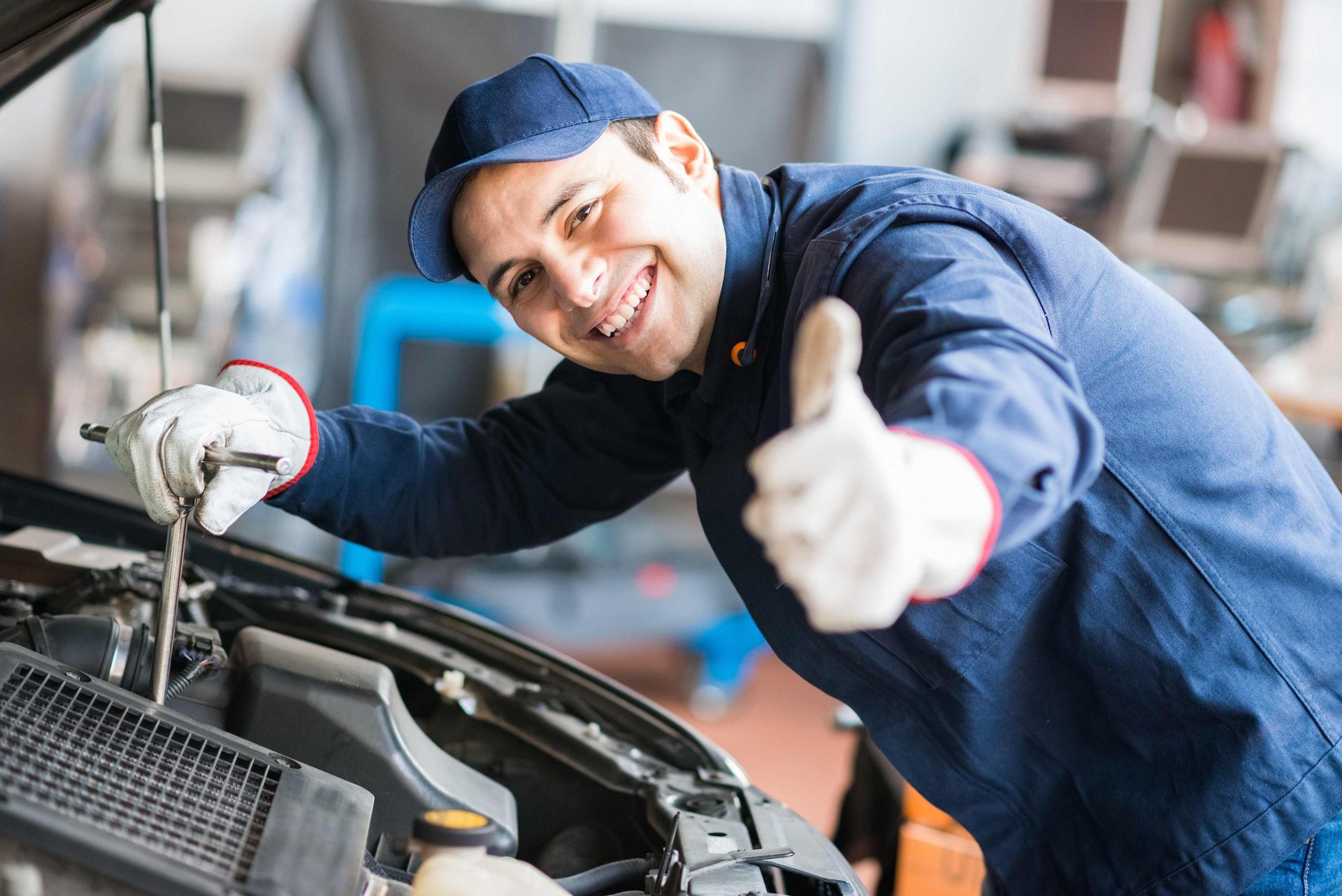 a smiling mechanic giving a thumbs up while working on a car