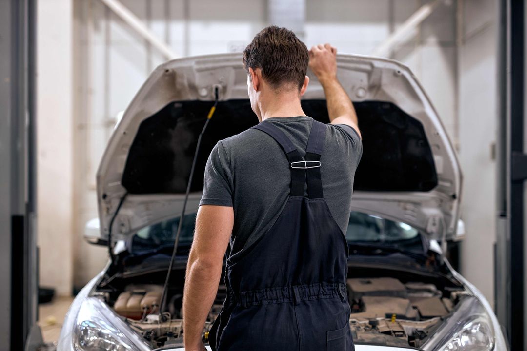 a man in overalls is looking under the hood of a car