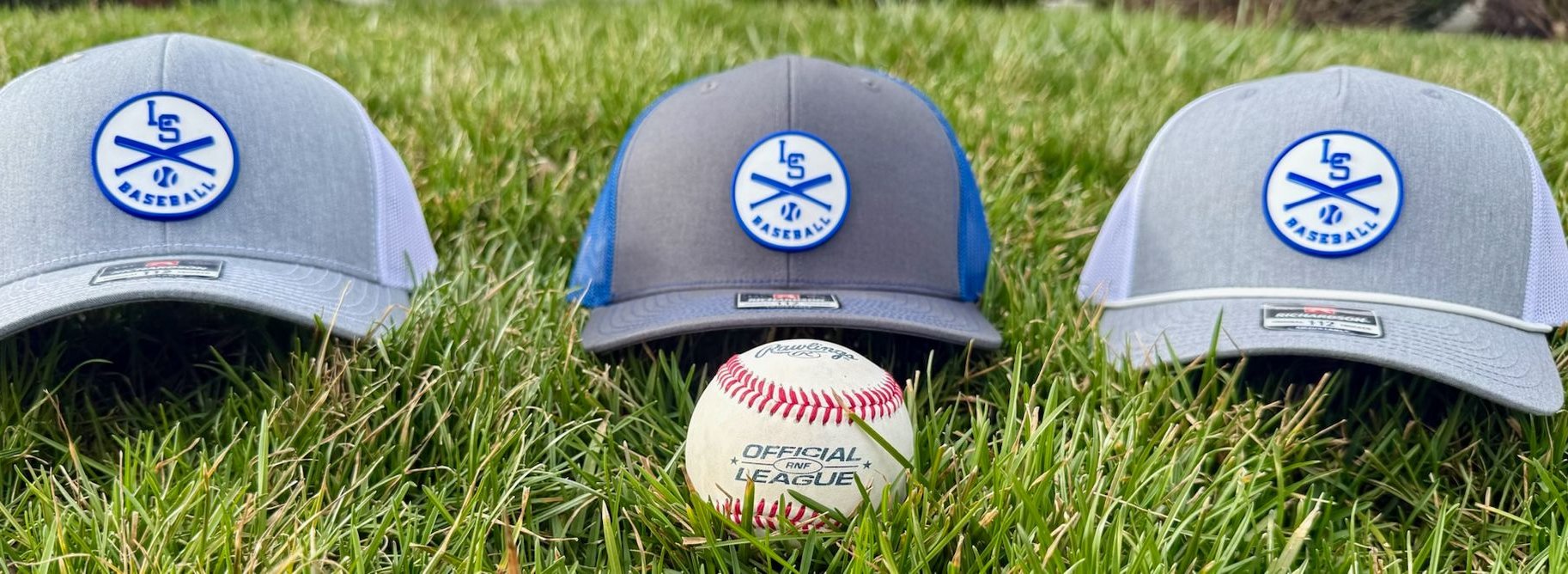 Three baseball caps with blue and white circular logos sit in a row on green grass behind a baseball.