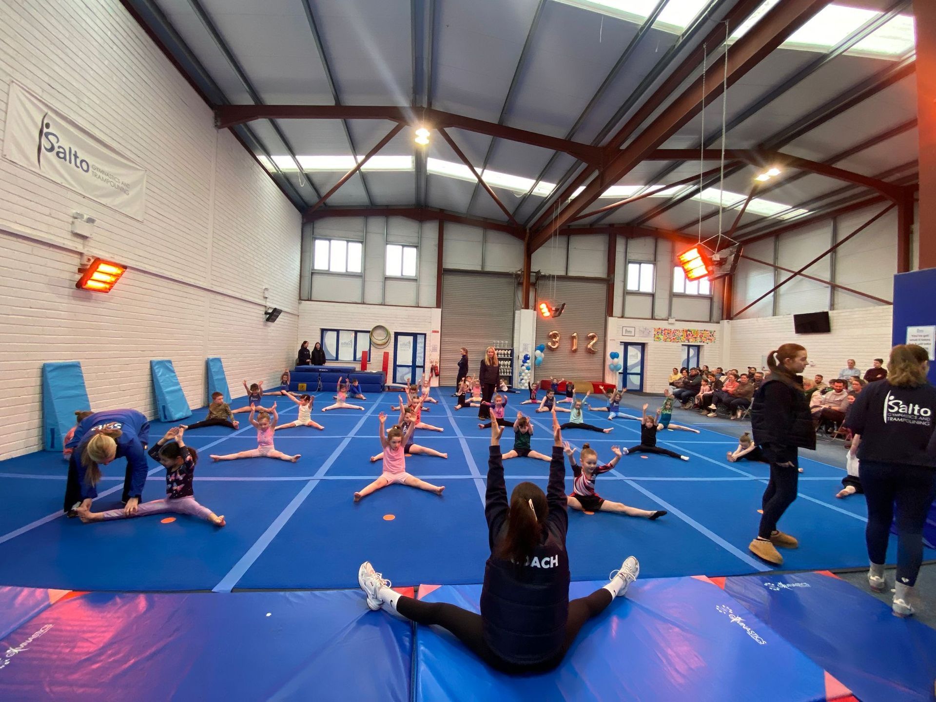 People stretching on blue mats in a gymnasium during a group fitness class