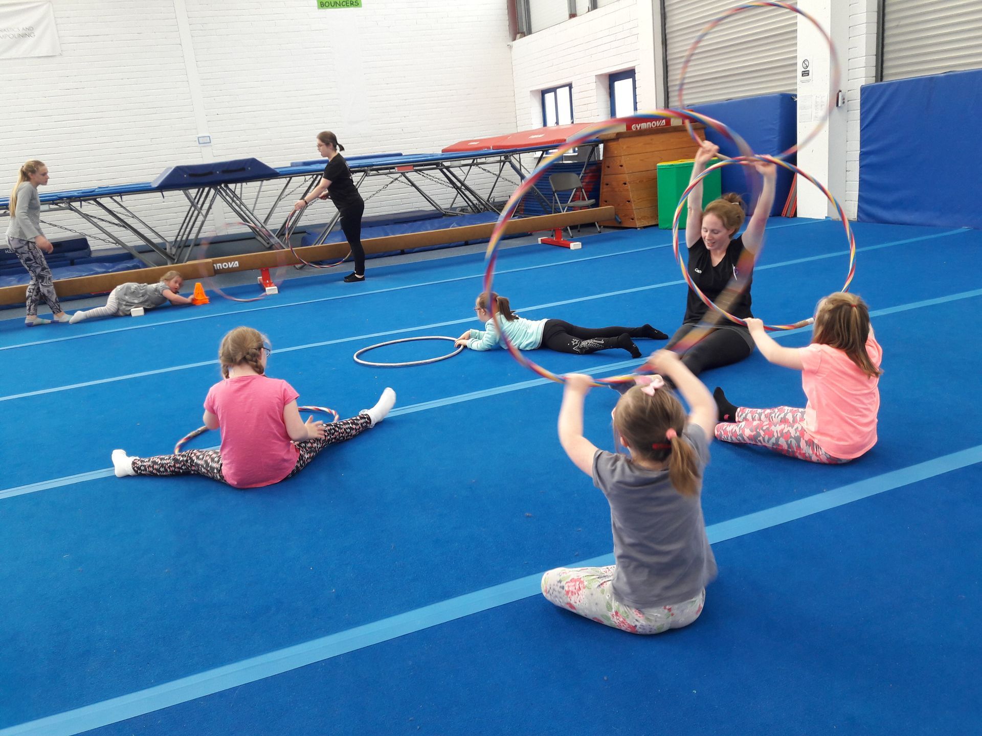 Children stretching with hoops on a blue gym mat during a gymnastics class