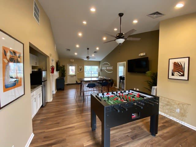 Interior community lounge with a foosball table, seating, and a wall-mounted TV.